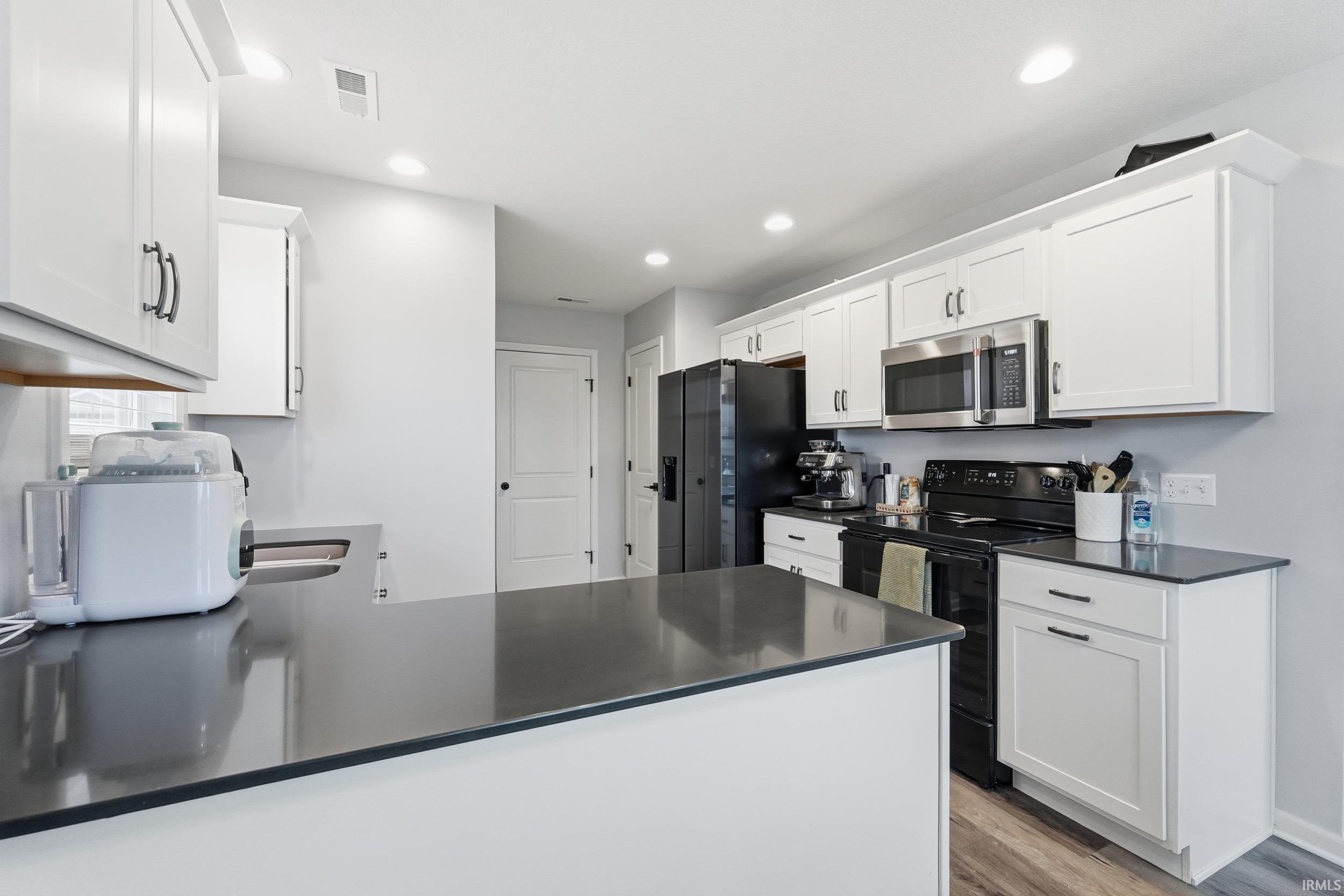 Kitchen featuring black appliances, a peninsula, white cabinetry, light wood-type flooring, and recessed lighting