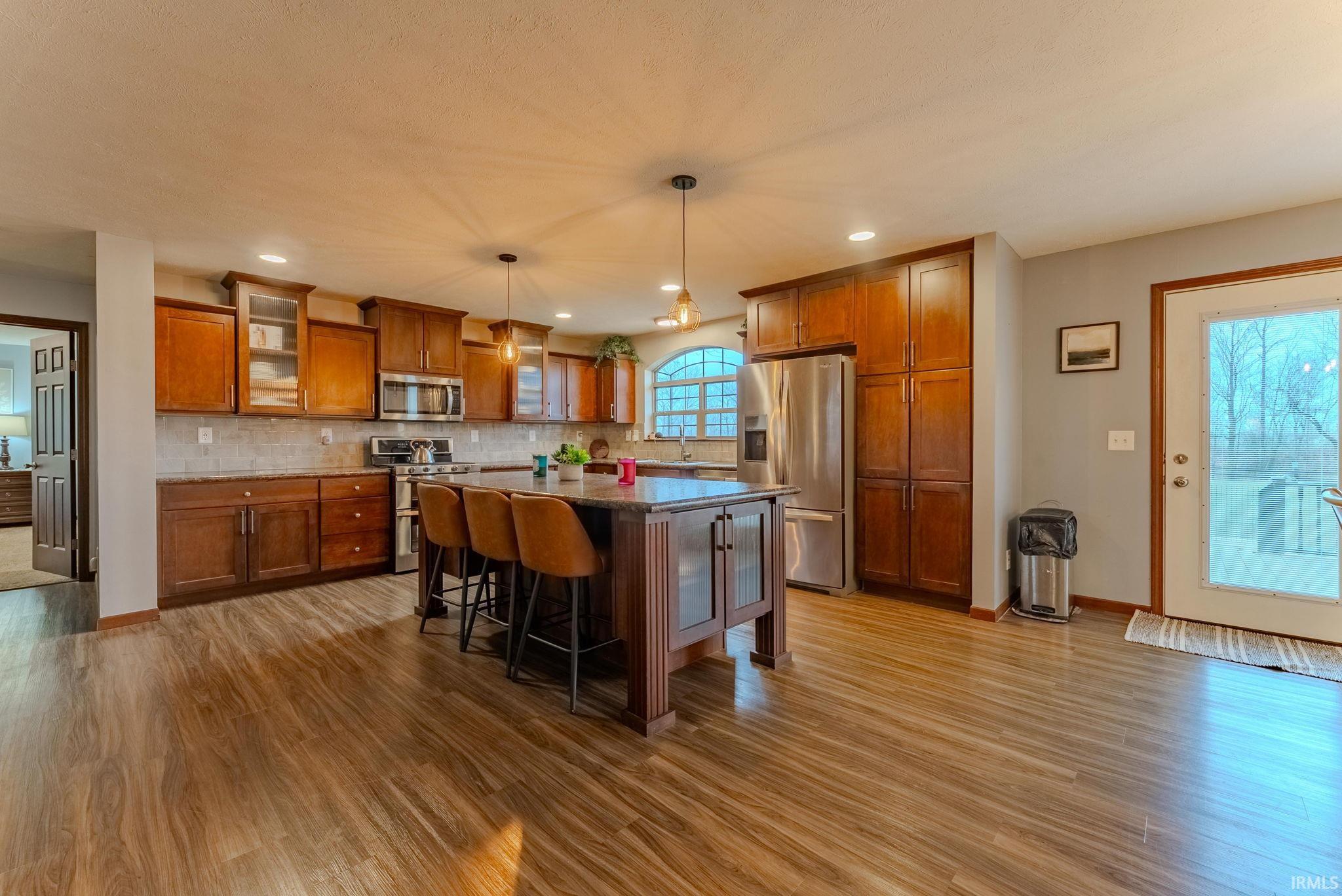 Kitchen featuring brown cabinetry, a kitchen bar, glass insert cabinets, appliances with stainless steel finishes, and a center island