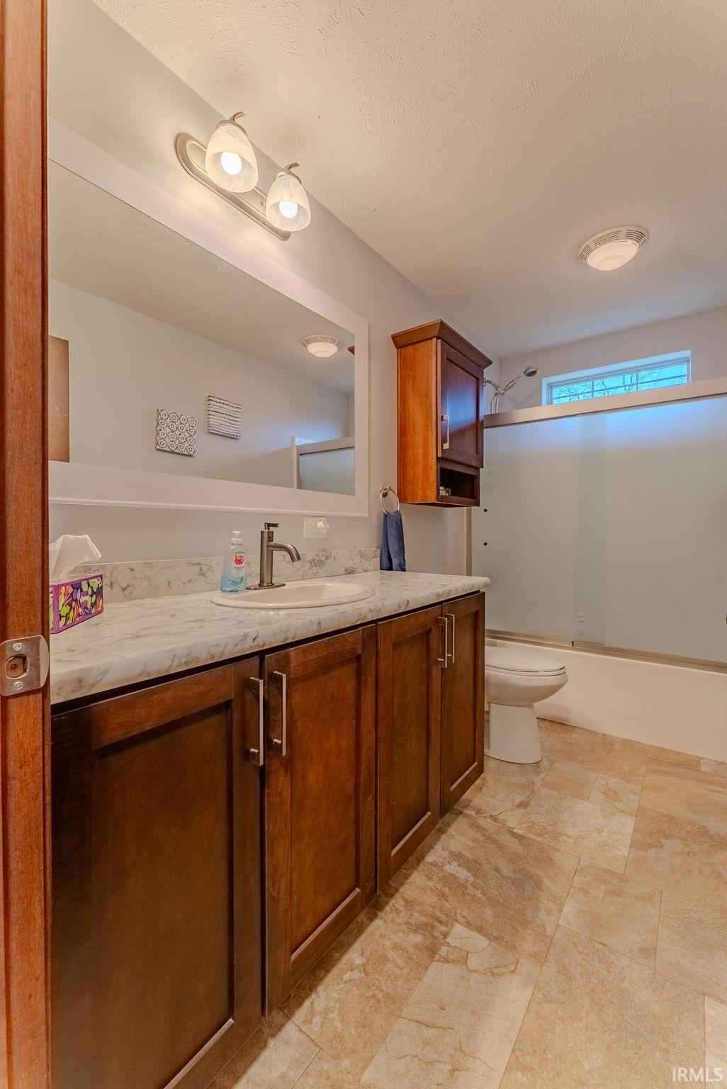 Full bath featuring vanity, bath / shower combo with glass door, and a textured ceiling