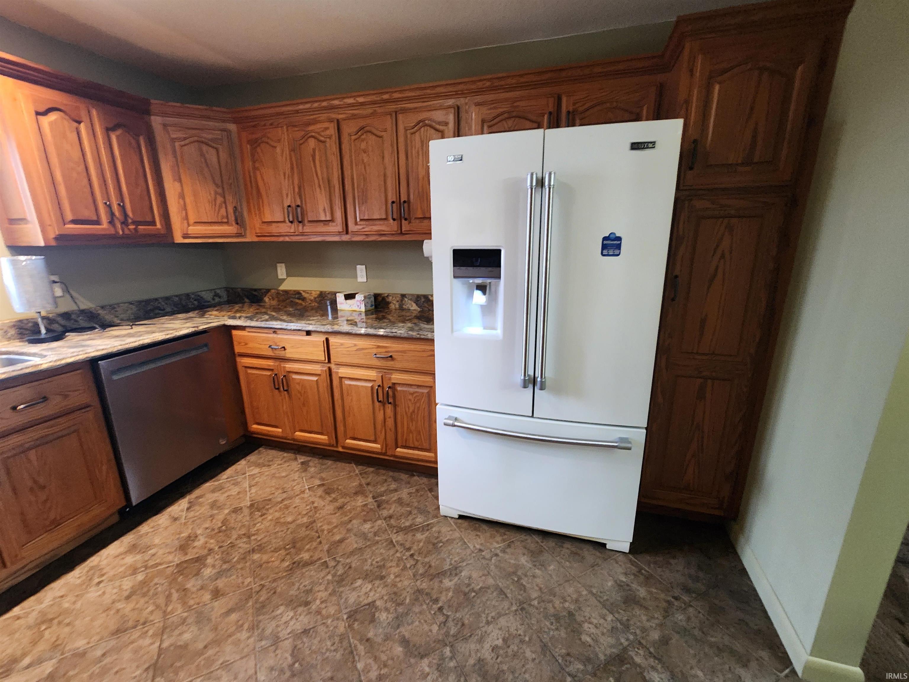 Kitchen with high end white refrigerator, brown cabinetry, light stone counters, and dishwasher