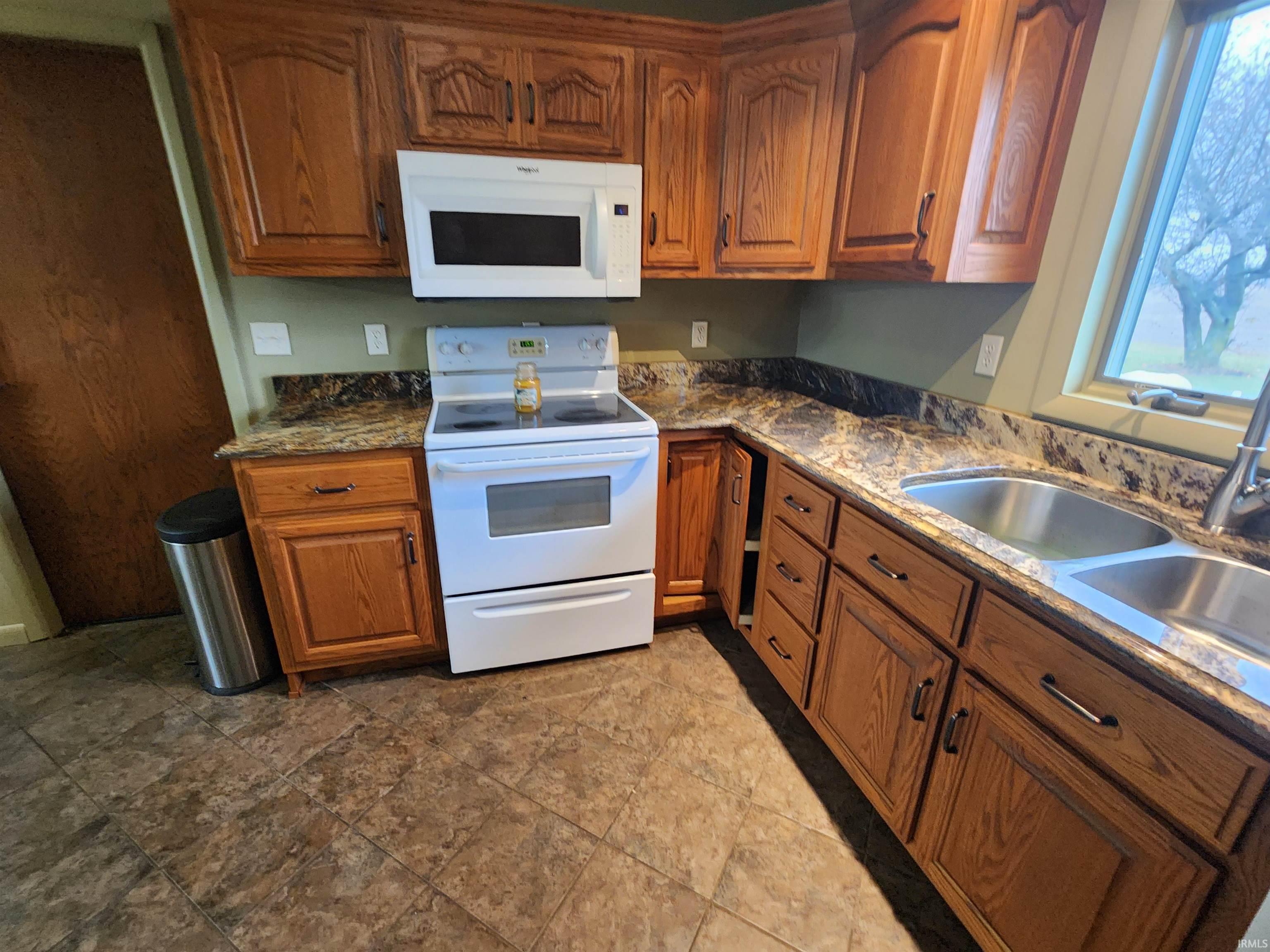 Kitchen with brown cabinetry, white appliances, and dark stone counters