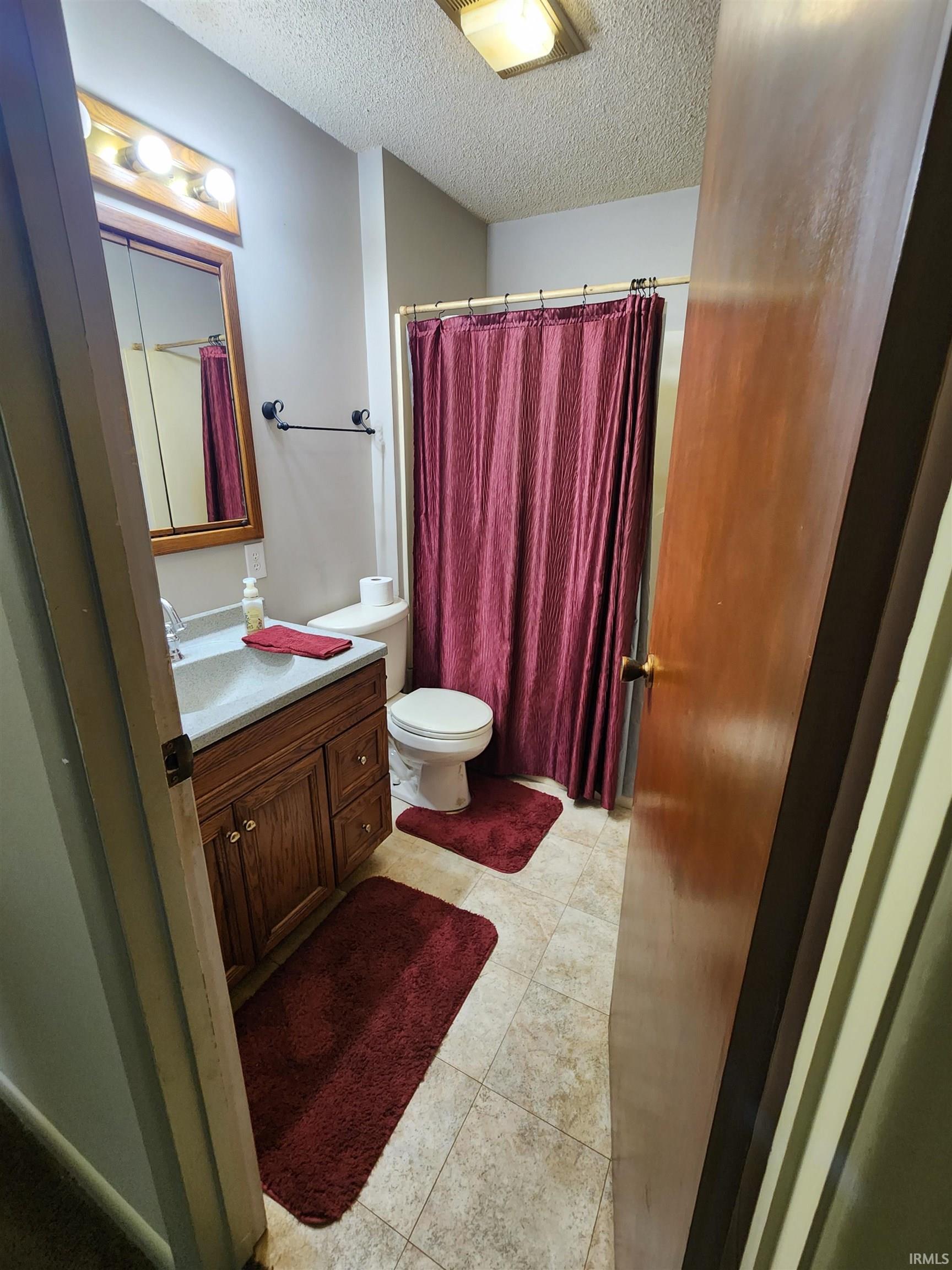 Bathroom with vanity, a shower with curtain, a textured ceiling, and light tile patterned flooring