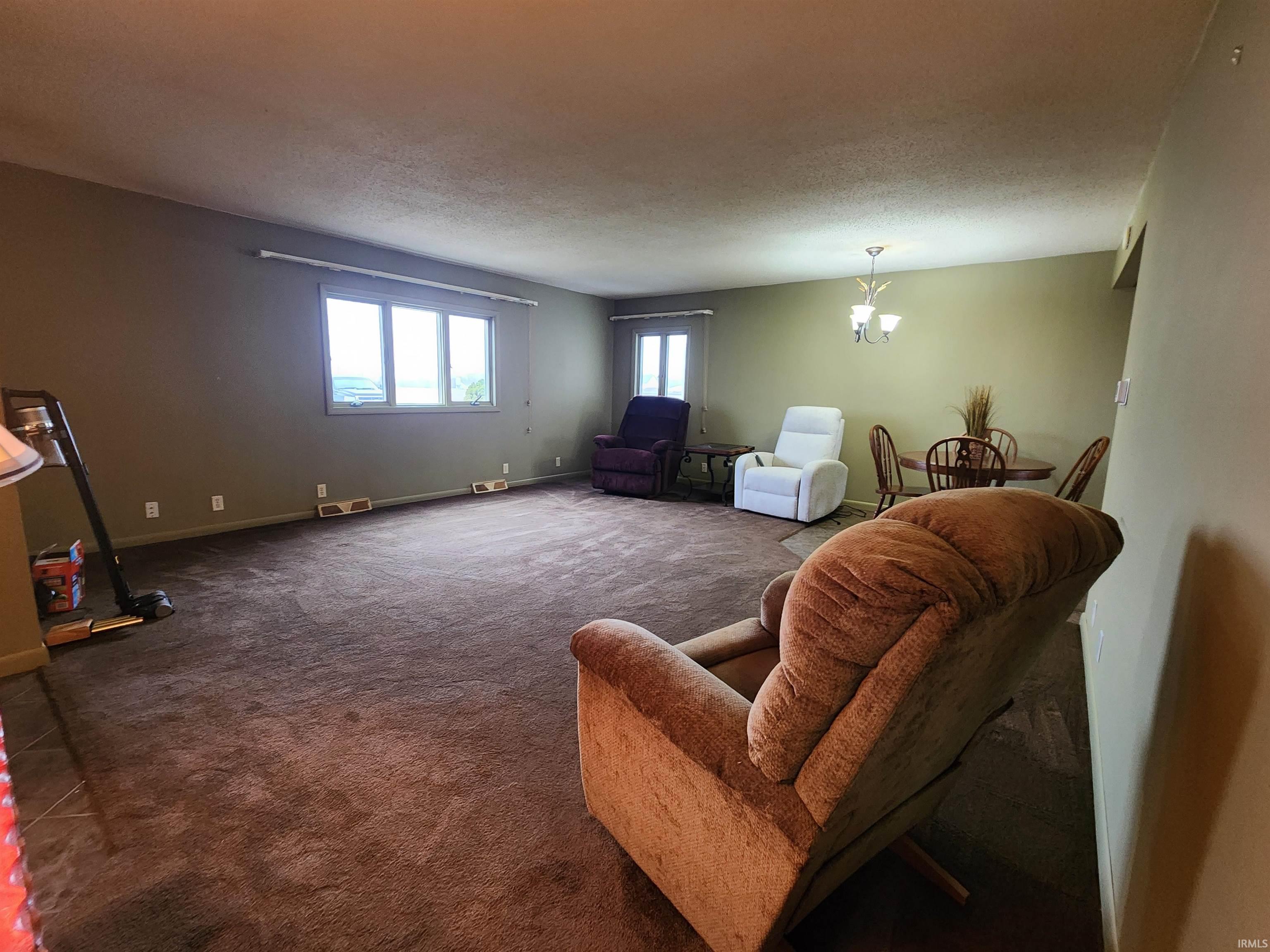 Living area featuring carpet flooring, a chandelier, and a textured ceiling