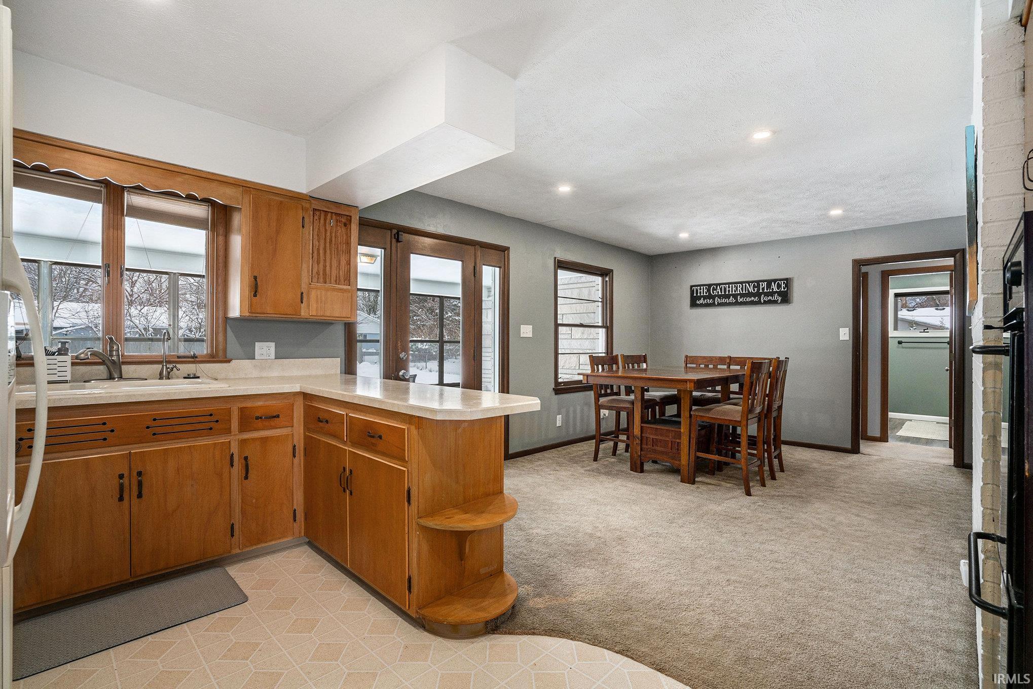 Kitchen with brown cabinetry, light countertops, a peninsula, open shelves, and light colored carpet