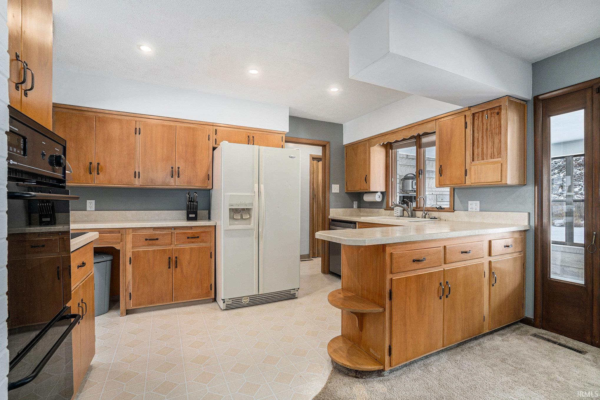 Kitchen featuring light floors, a peninsula, white fridge with ice dispenser, light countertops, and brown cabinets
