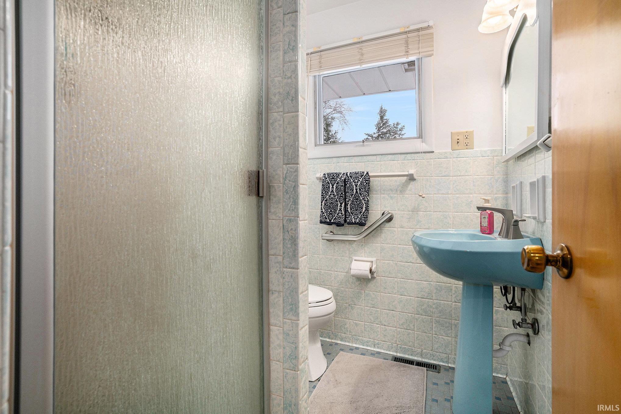 Full bath featuring a shower stall, tile walls, and wainscoting