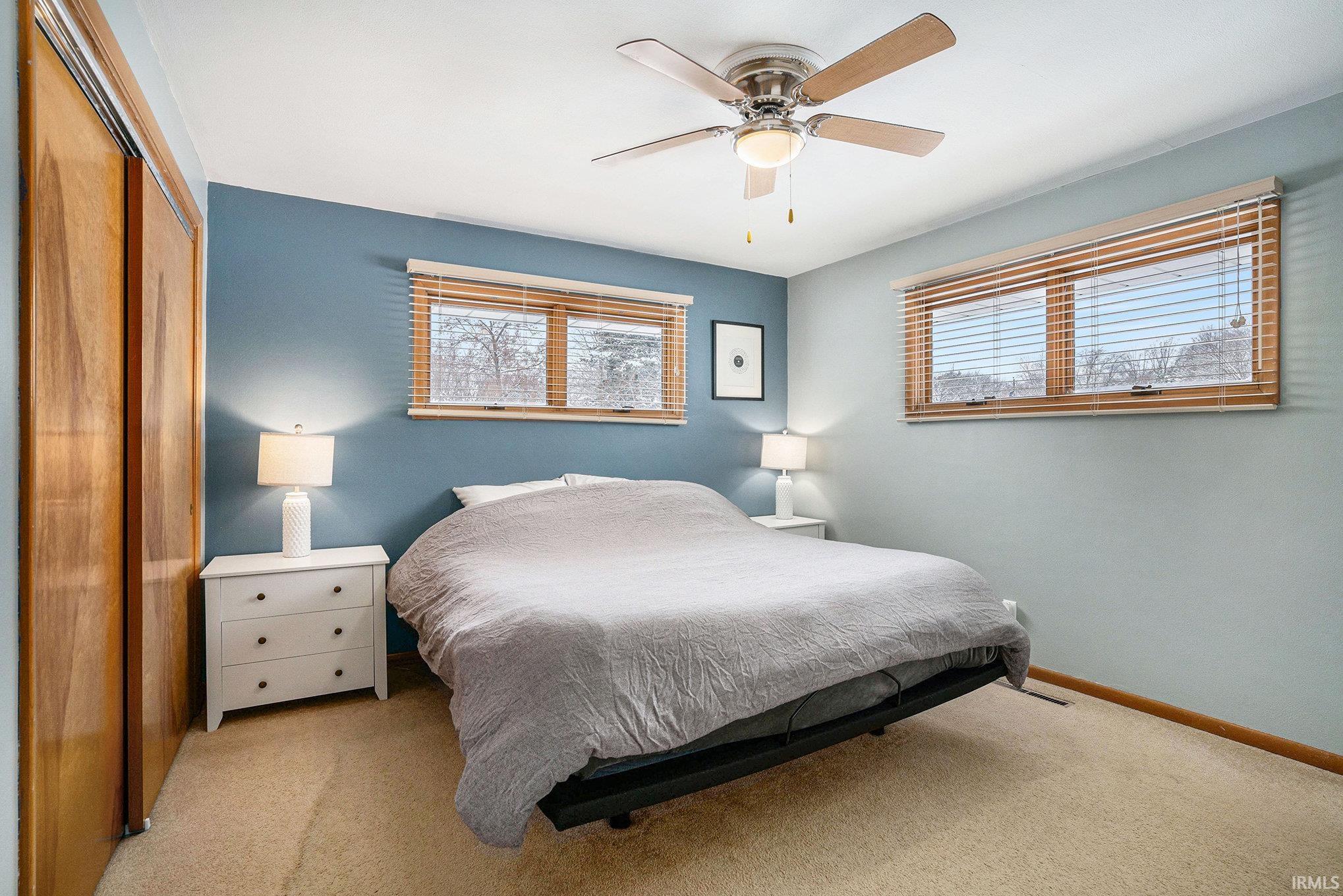 Carpeted bedroom featuring a closet, multiple windows, and a ceiling fan