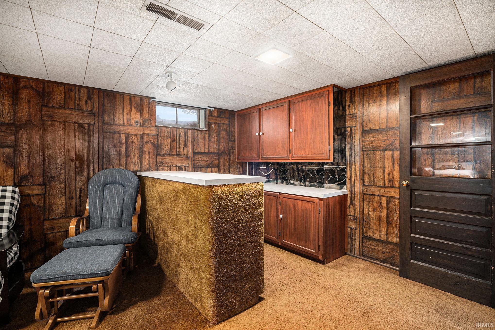 Bar area featuring light colored carpet, light countertops, wood walls, and brown cabinetry