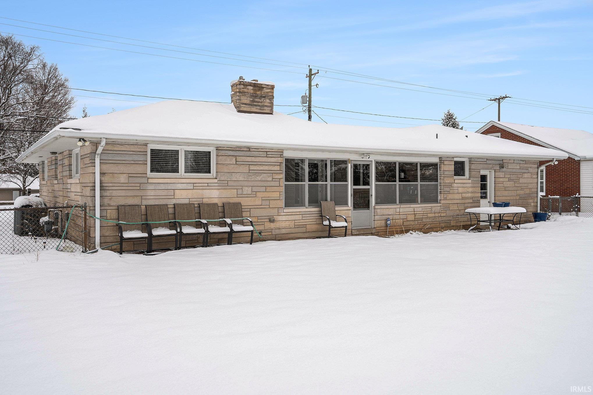 Snow covered back of property with stone siding and a chimney