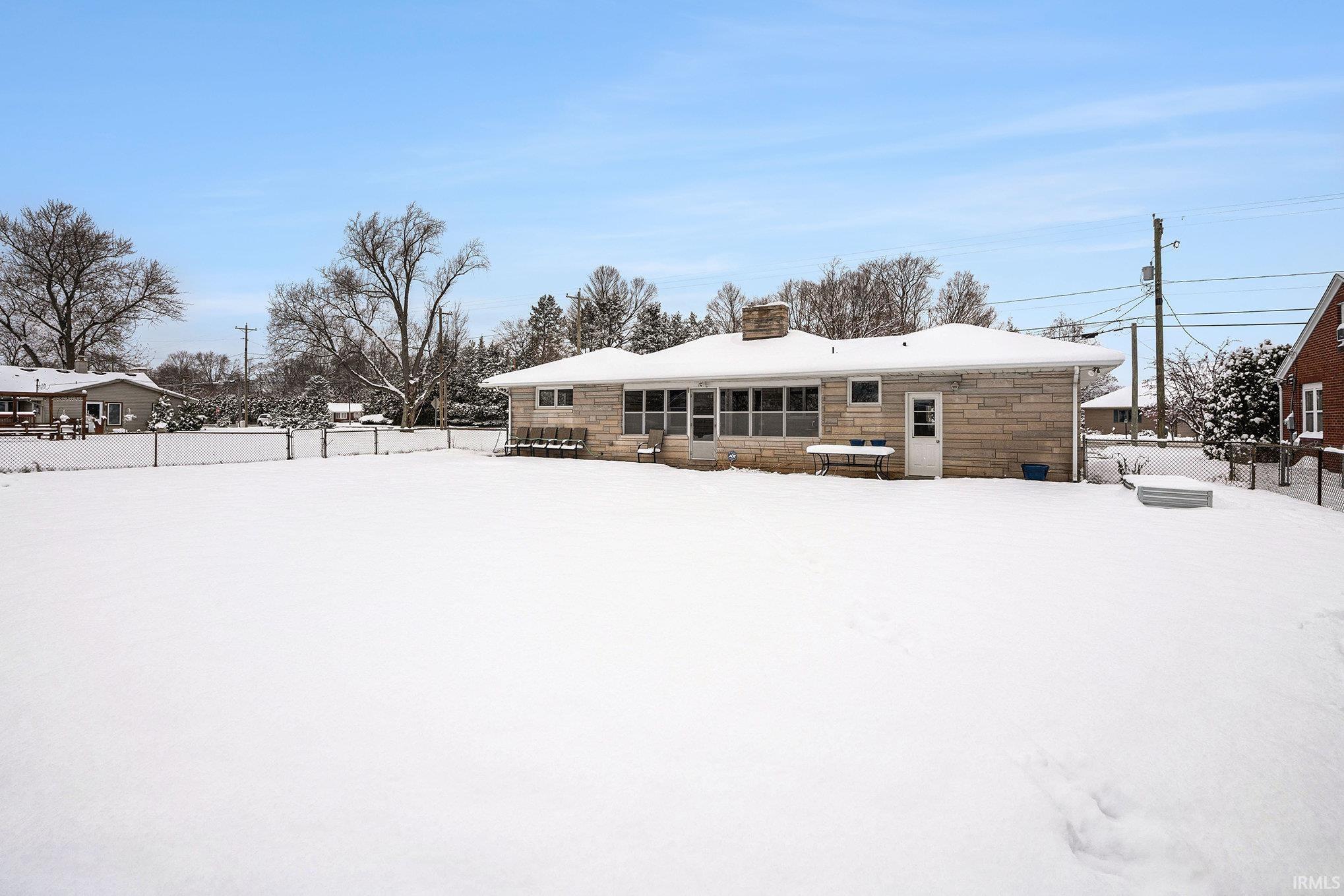 Snow covered property with a chimney and stone siding