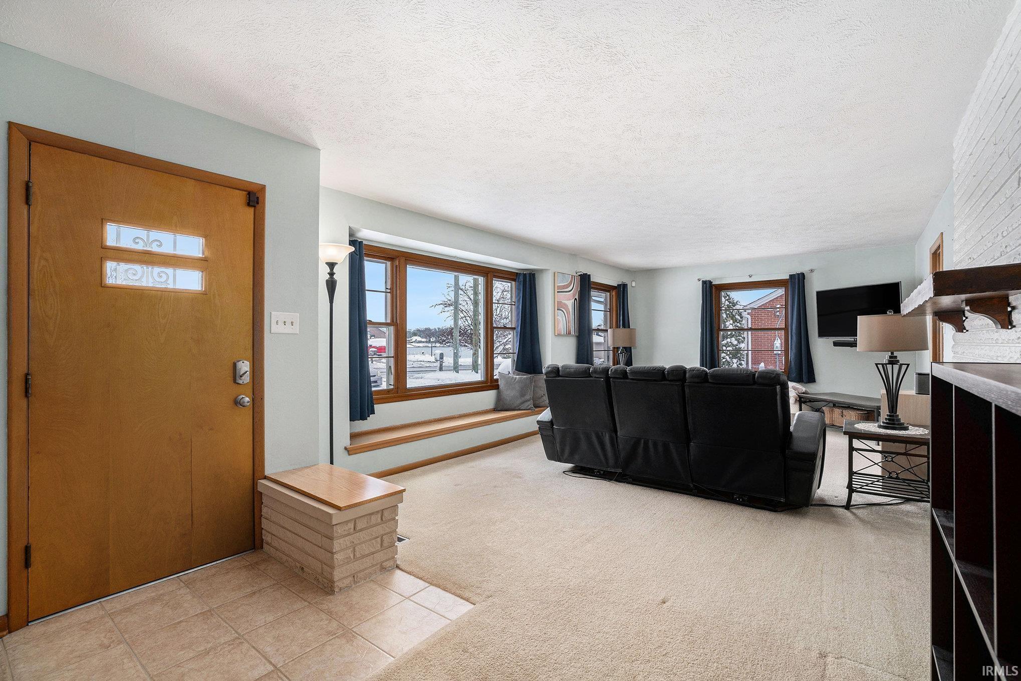 Living room with plenty of natural light, light colored carpet, a textured ceiling, and light tile patterned flooring