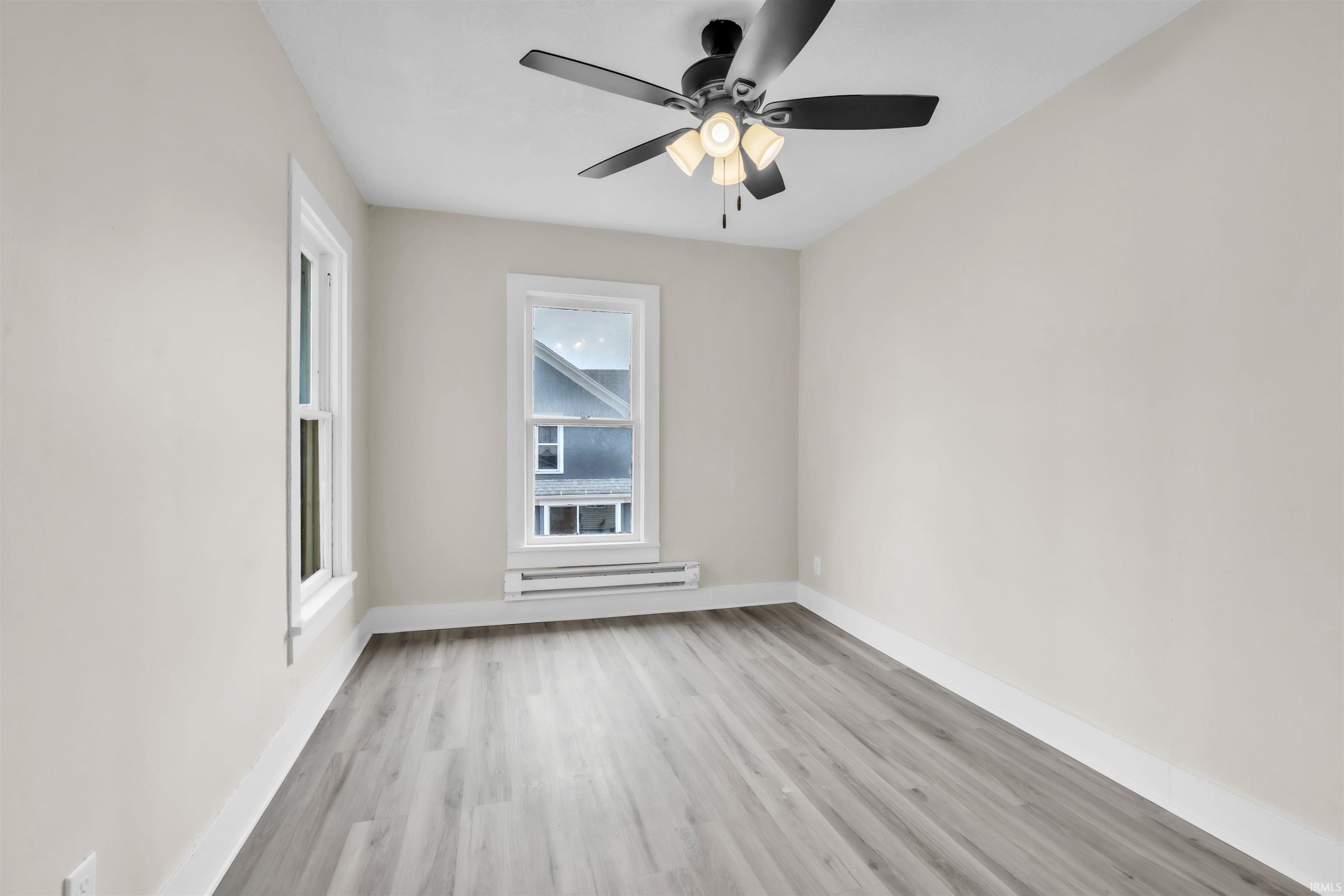 Empty room featuring light wood-type flooring, baseboard heating, and a ceiling fan