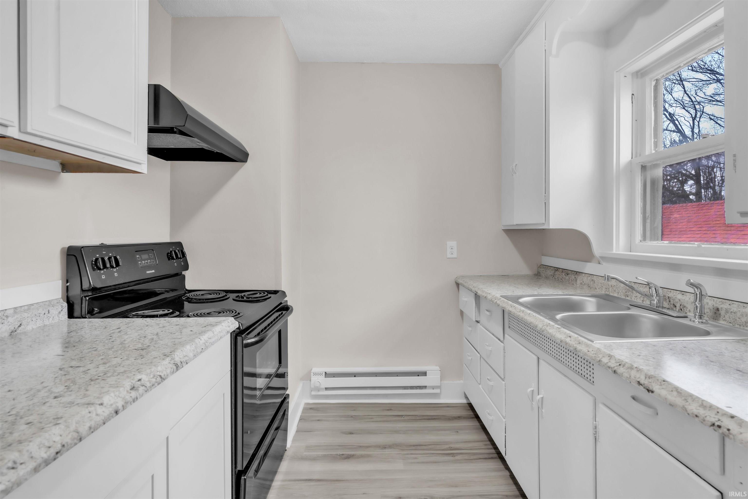 Kitchen with black range with electric cooktop, white cabinetry, range hood, and light countertops