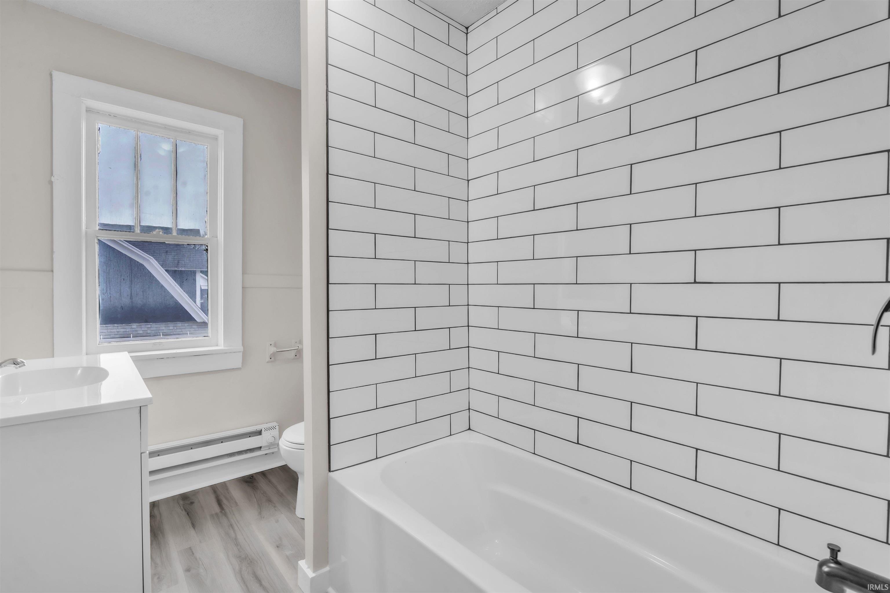 Bathroom with vanity, a baseboard heating unit, bathing tub / shower combination, and light wood-type flooring