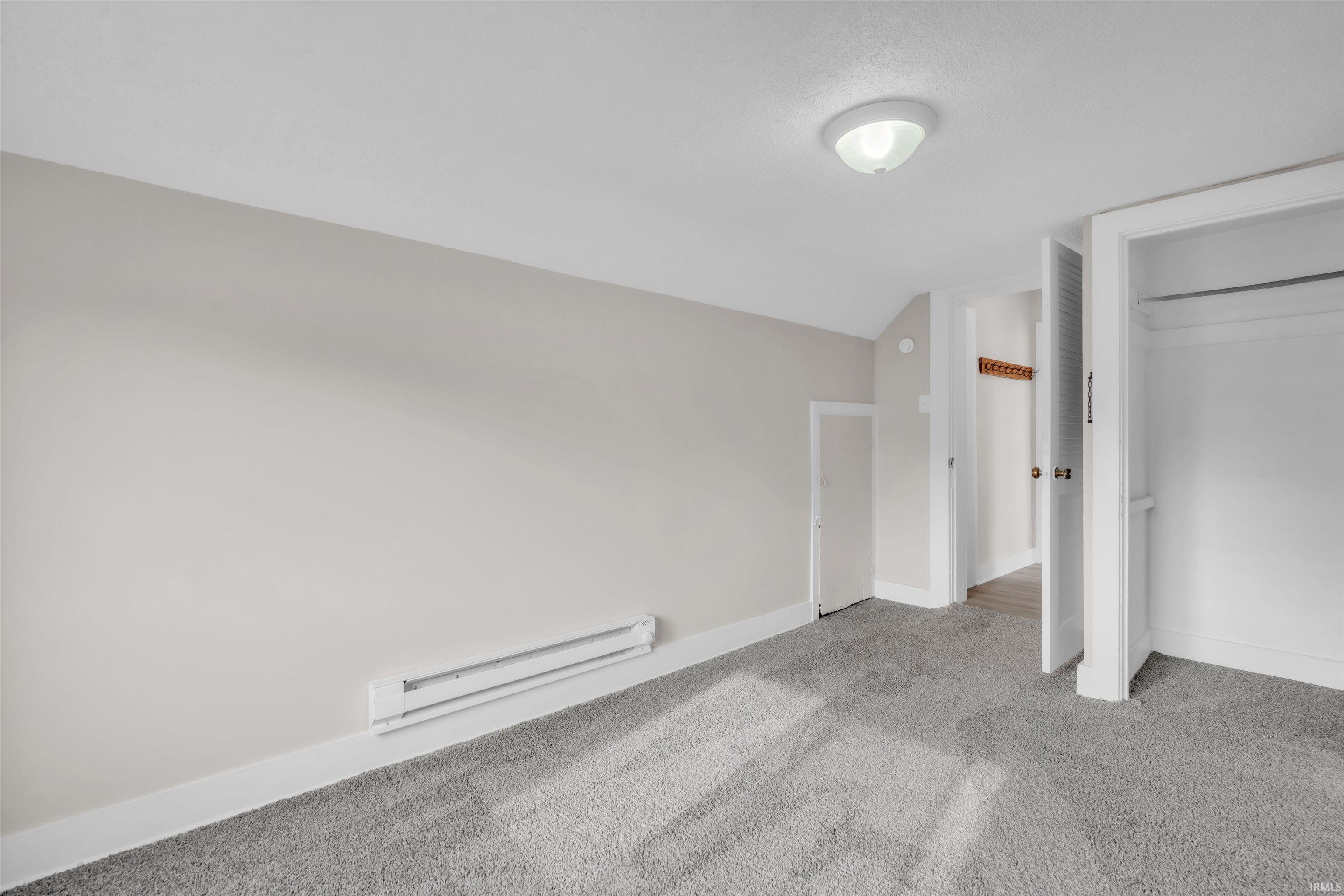 Unfurnished bedroom featuring vaulted ceiling, baseboard heating, carpet, and a closet