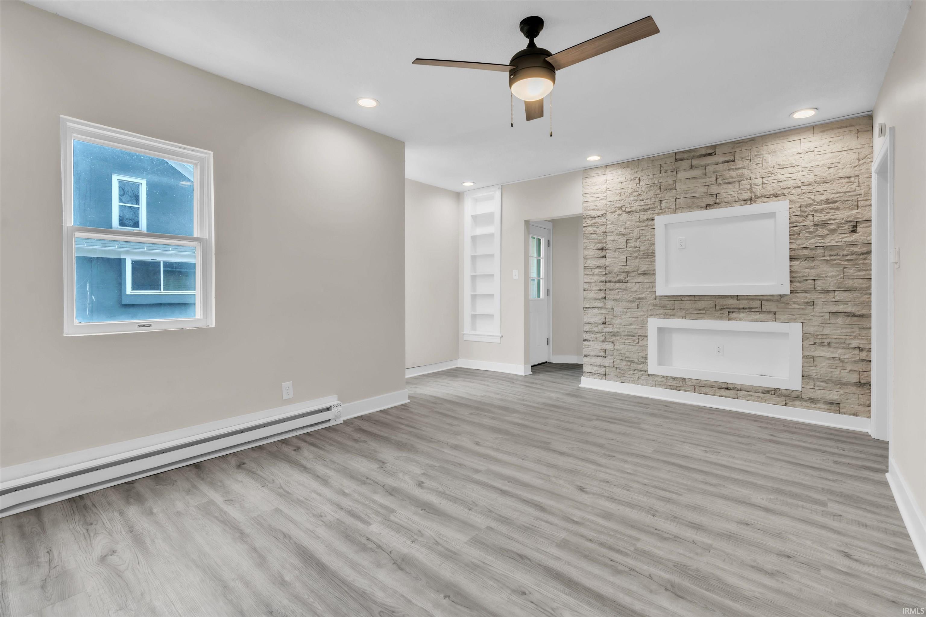 Unfurnished living room featuring built in features, ceiling fan, a baseboard radiator, wood finished floors, and recessed lighting