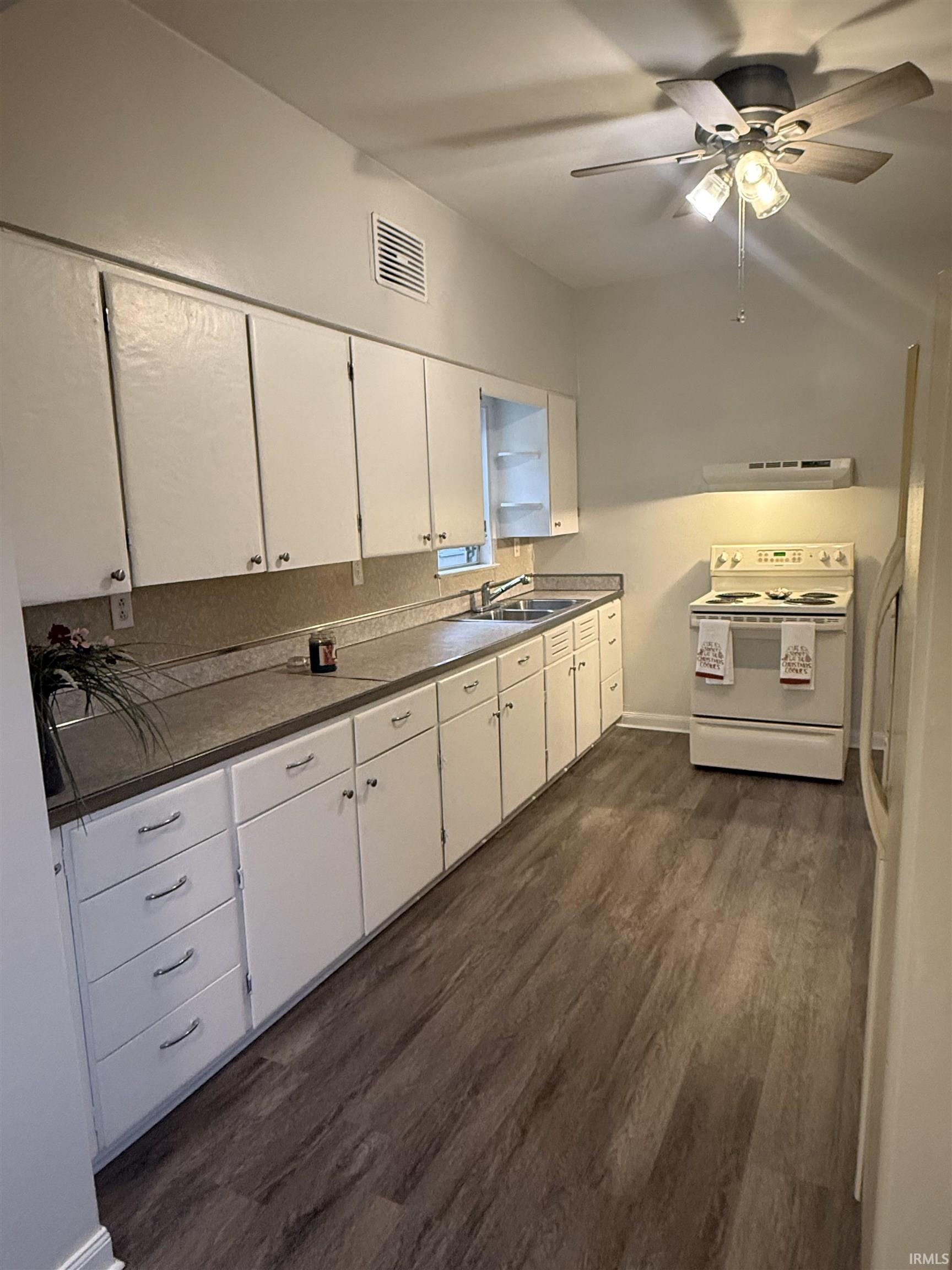 Kitchen with white appliances, dark wood-style floors, white cabinets, a ceiling fan, and range hood
