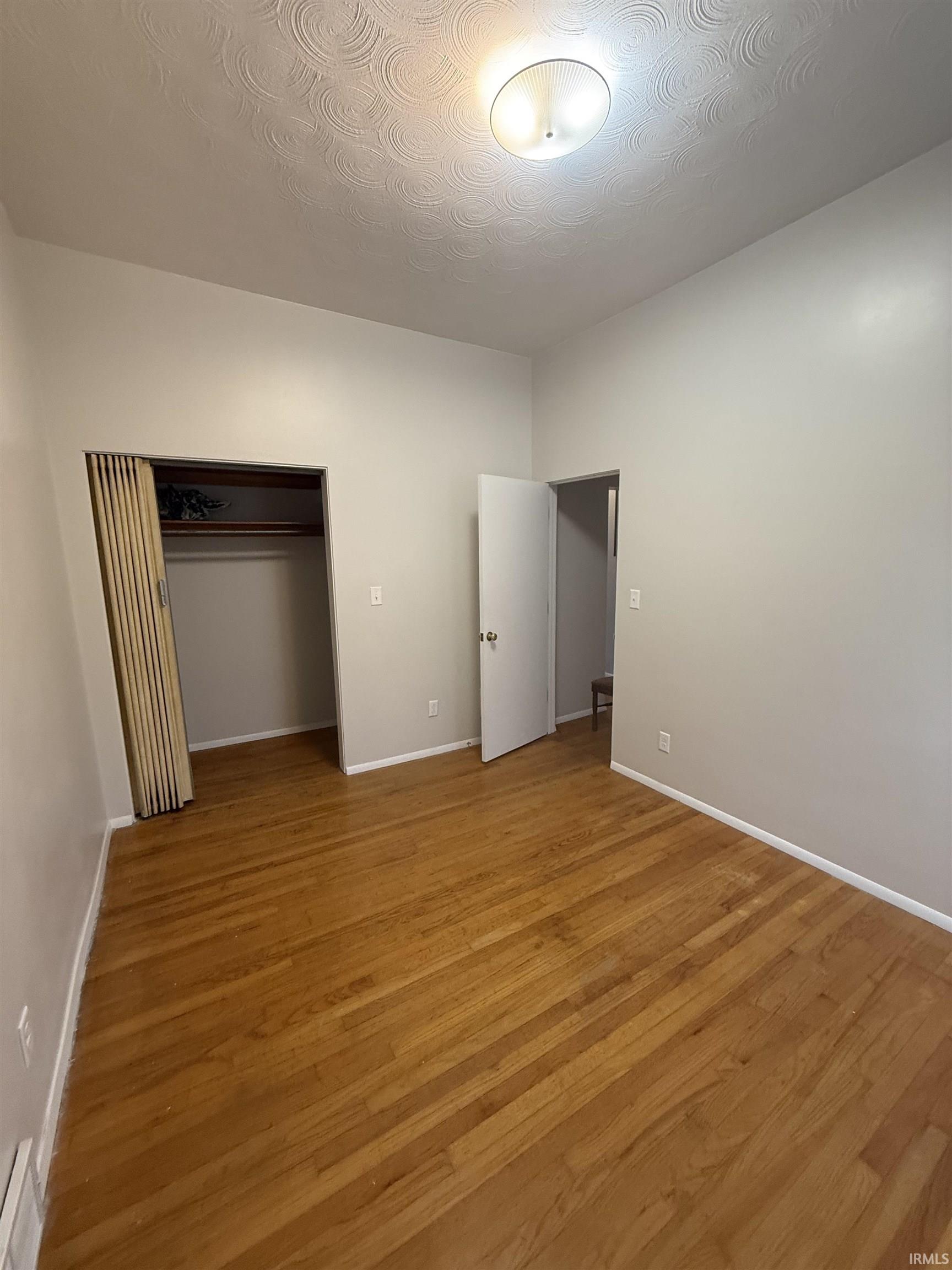 Unfurnished bedroom with a closet, light wood finished floors, and a textured ceiling