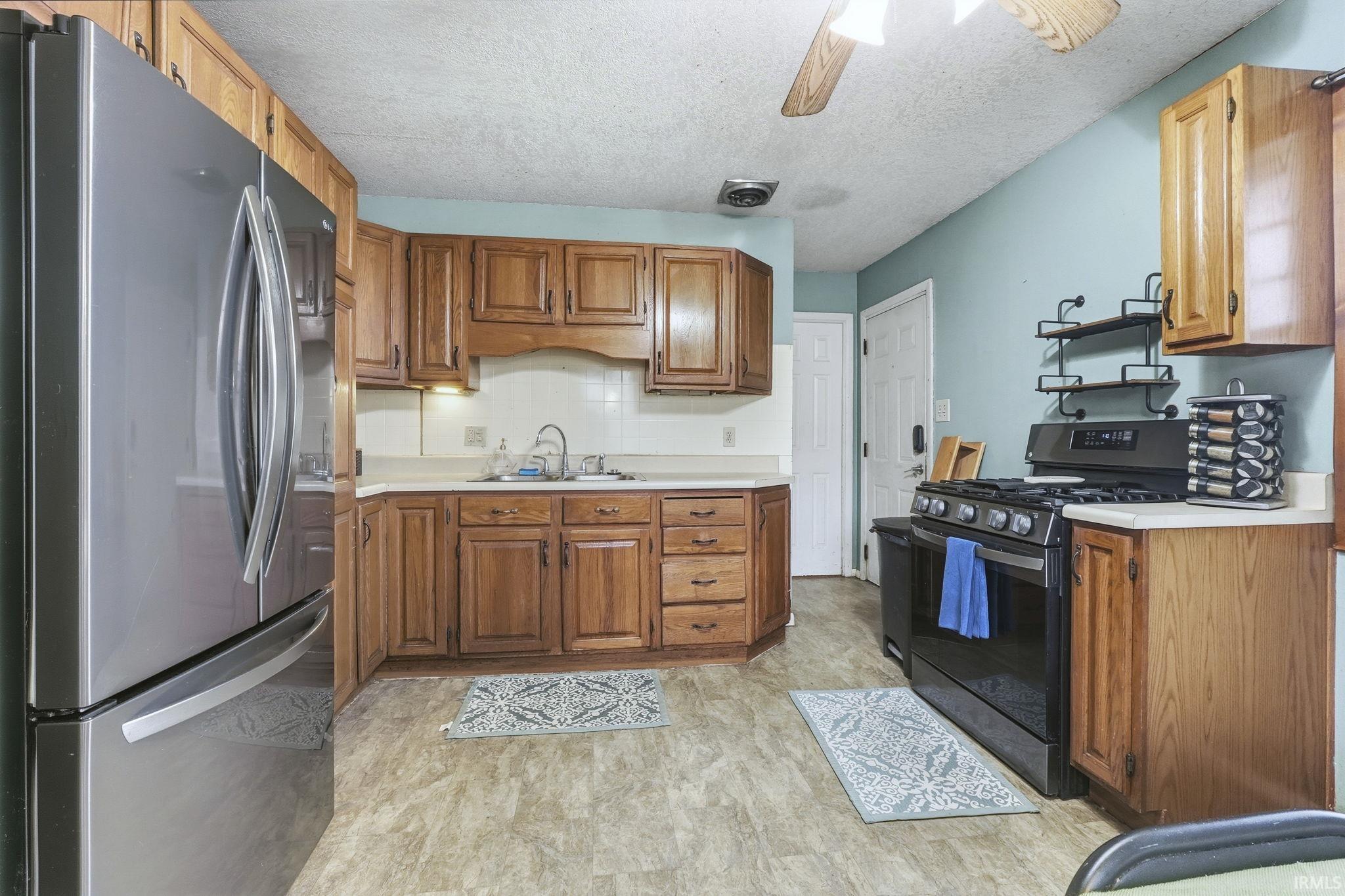 Kitchen featuring freestanding refrigerator, range with gas stovetop, light countertops, brown cabinetry, and a textured ceiling