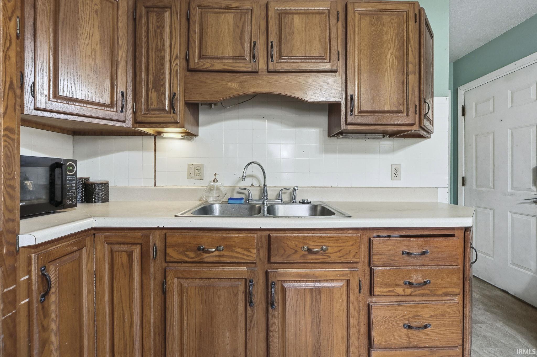 Kitchen with tasteful backsplash, light countertops, black microwave, and brown cabinetry