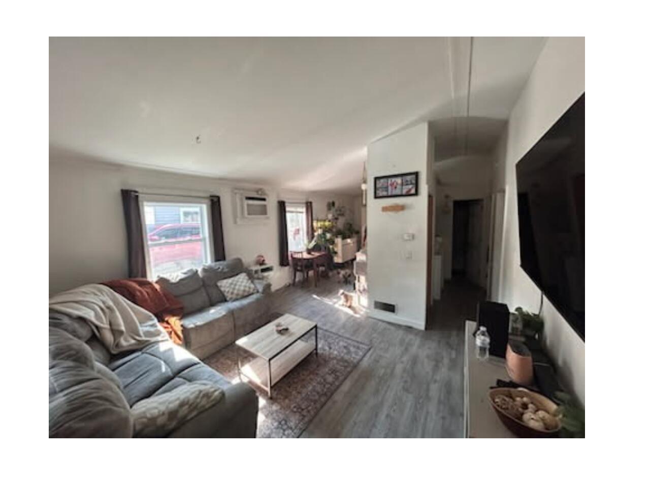 Living room with wood finished floors, lofted ceiling, and a wall mounted air conditioner
