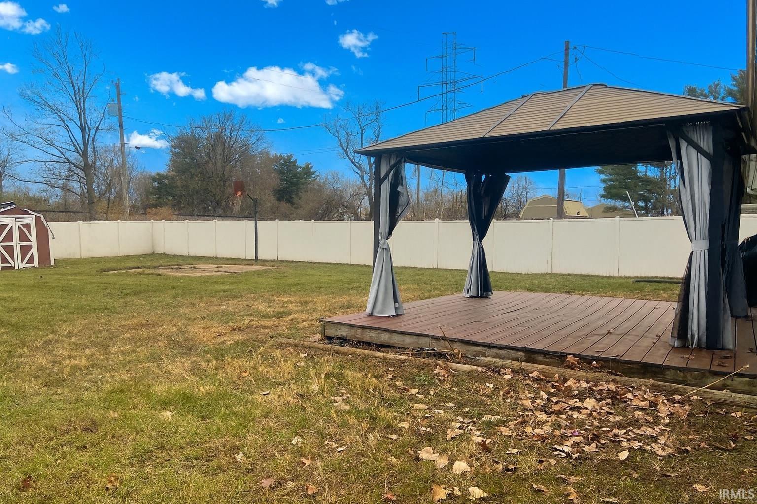 Fenced backyard featuring a wooden deck, a gazebo, and a storage unit