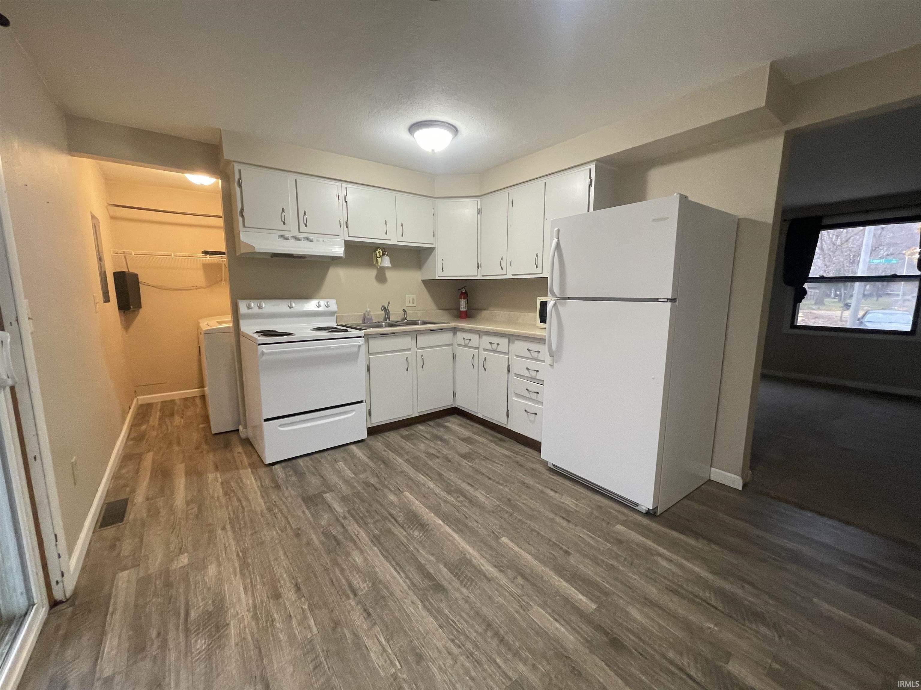 Kitchen featuring white appliances, light countertops, dark wood finished floors, white cabinetry, and under cabinet range hood