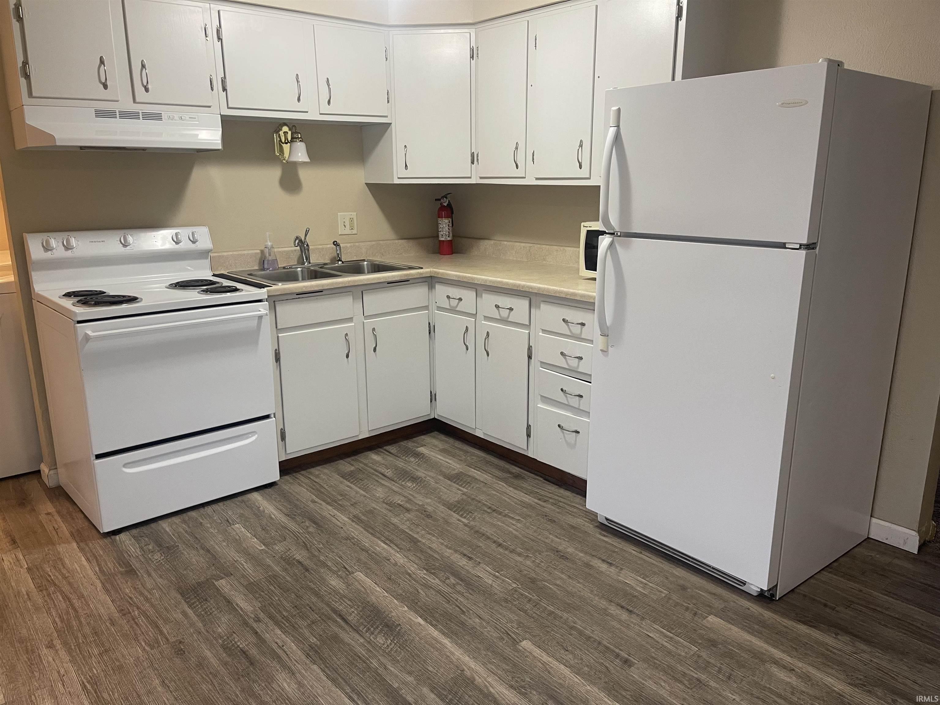 Kitchen featuring white appliances, light countertops, white cabinets, and dark wood-style floors
