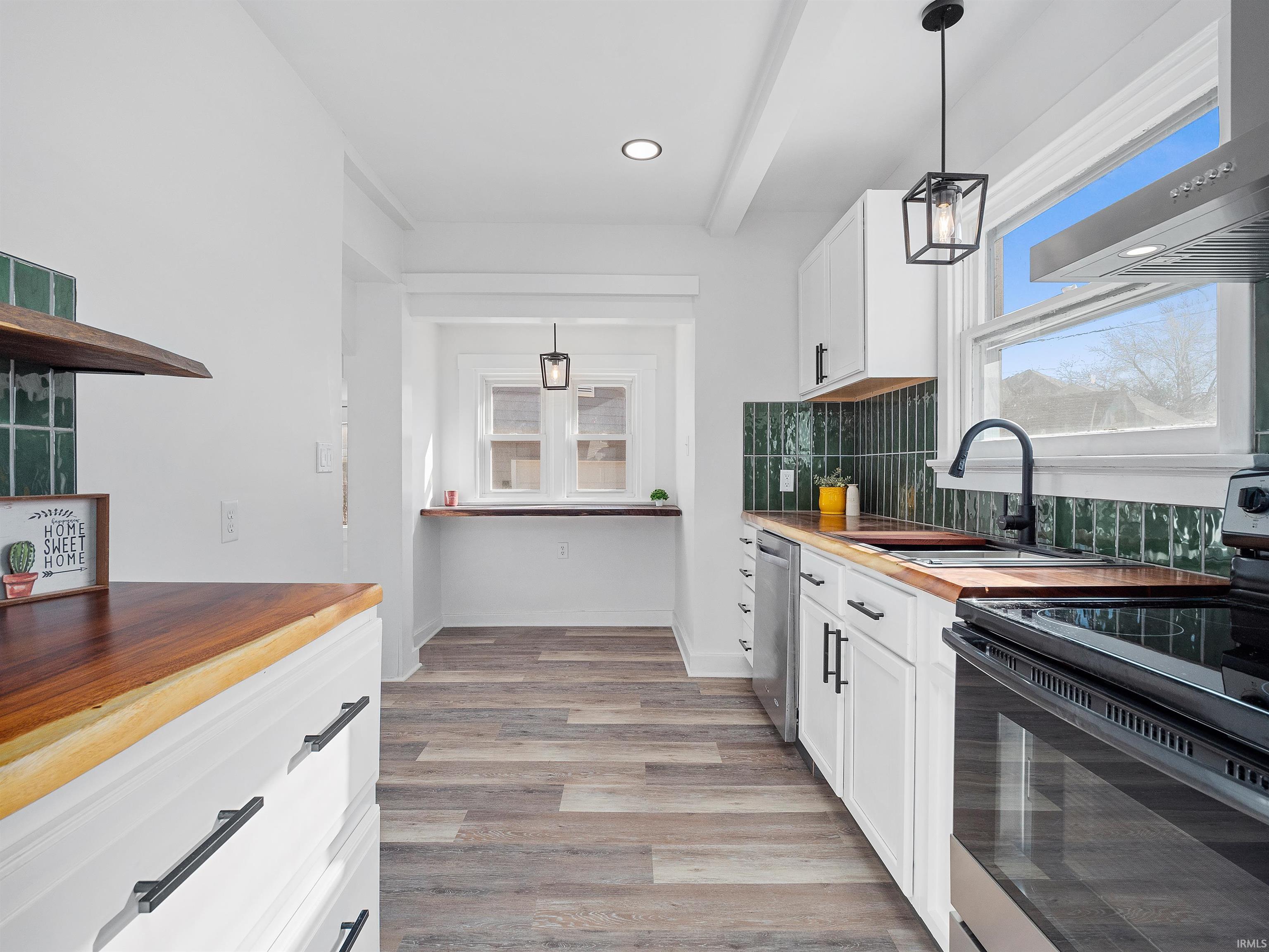 Kitchen with wooden counters, decorative light fixtures, range with electric cooktop, white cabinets, and recessed lighting