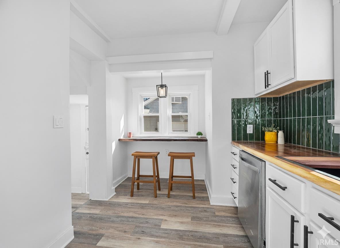 Kitchen with light wood-style flooring, white cabinetry, dishwasher, backsplash, and pendant lighting