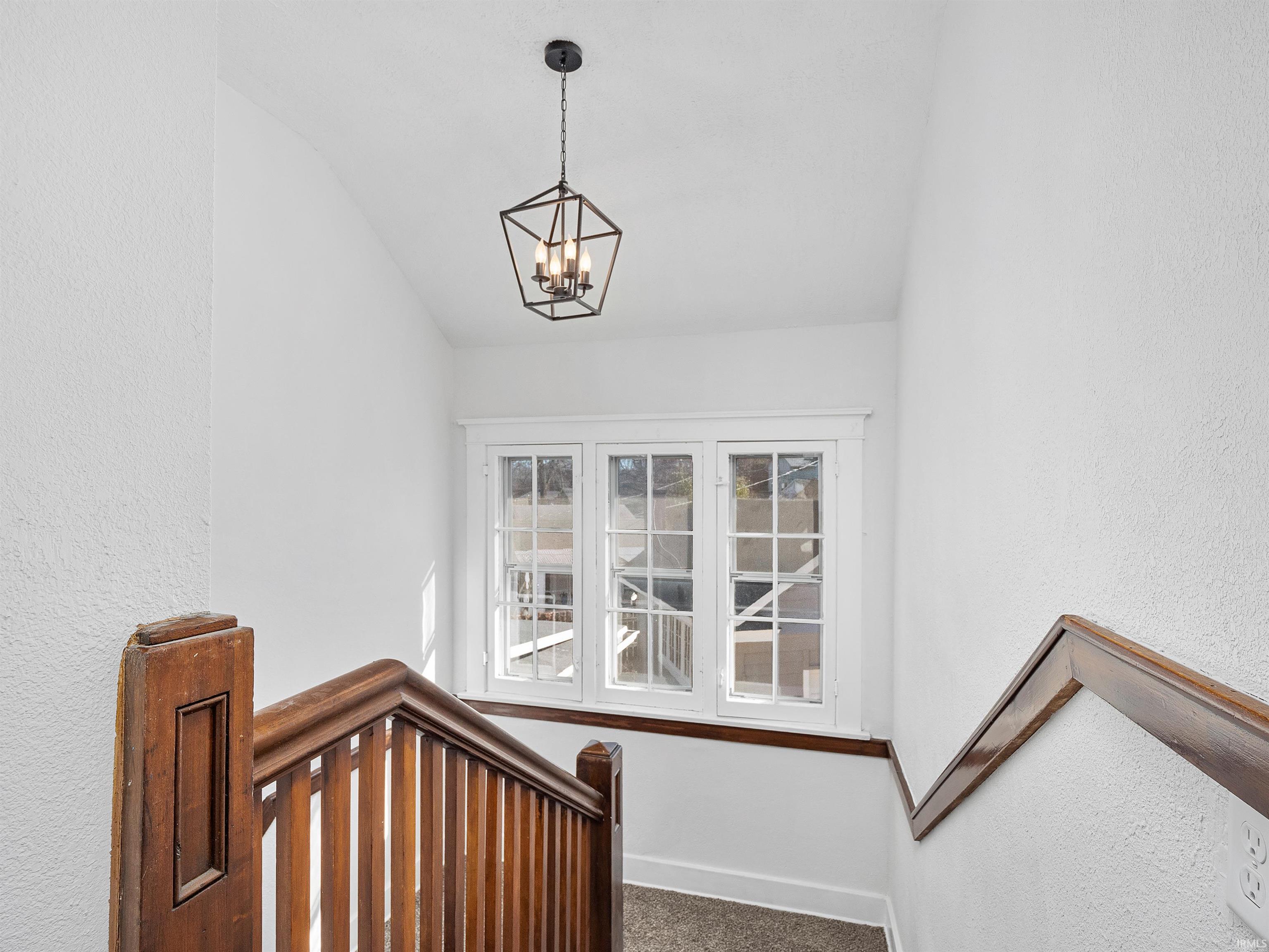 Stairway with a textured wall, vaulted ceiling, a chandelier, and carpet