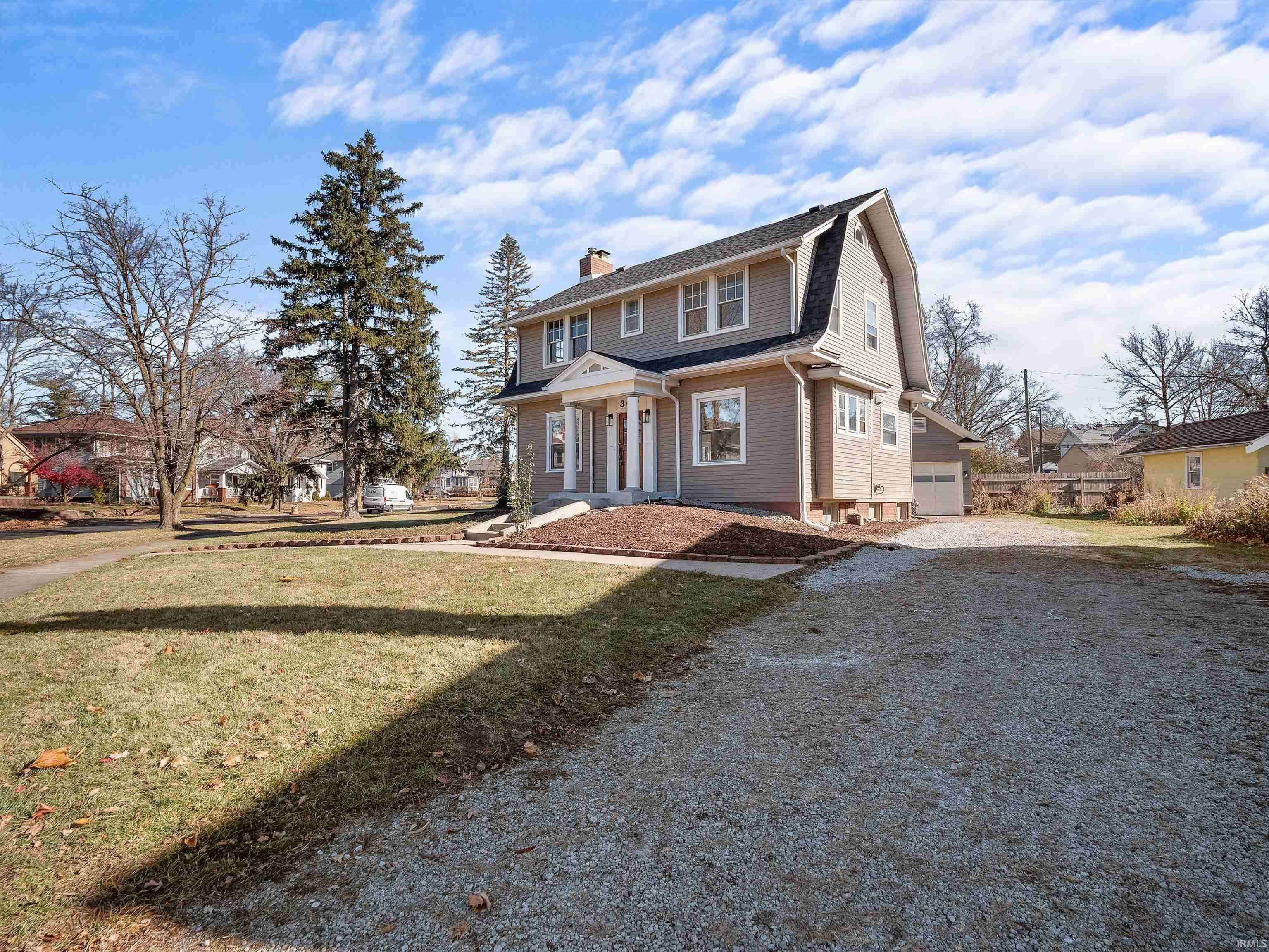 Dutch colonial with a gambrel roof, gravel driveway, a front yard, a chimney, and a garage