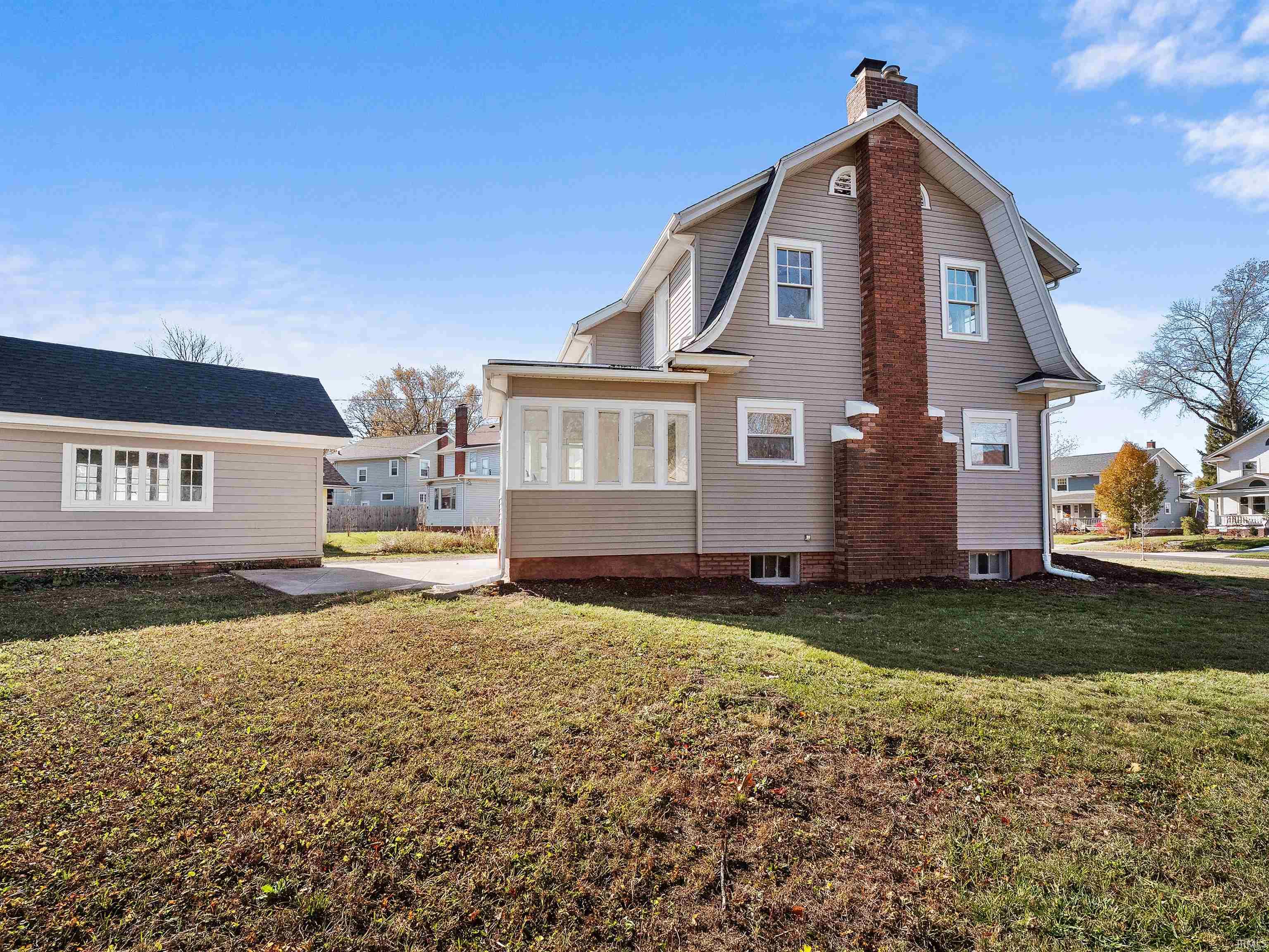 Back of house featuring a yard, a chimney, a sunroom, and a patio
