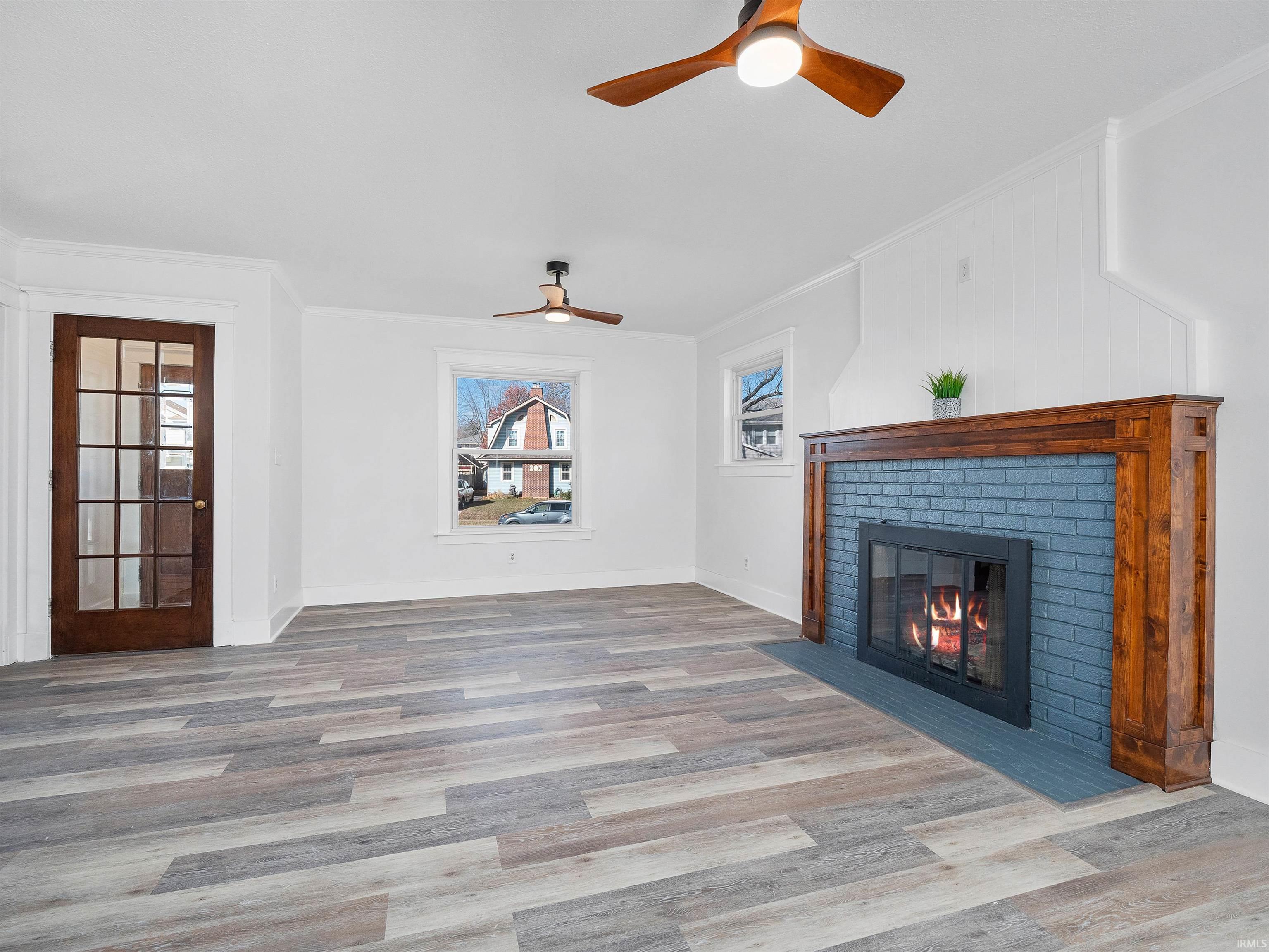 Unfurnished living room featuring ornamental molding, light wood-style flooring, a brick fireplace, and ceiling fan