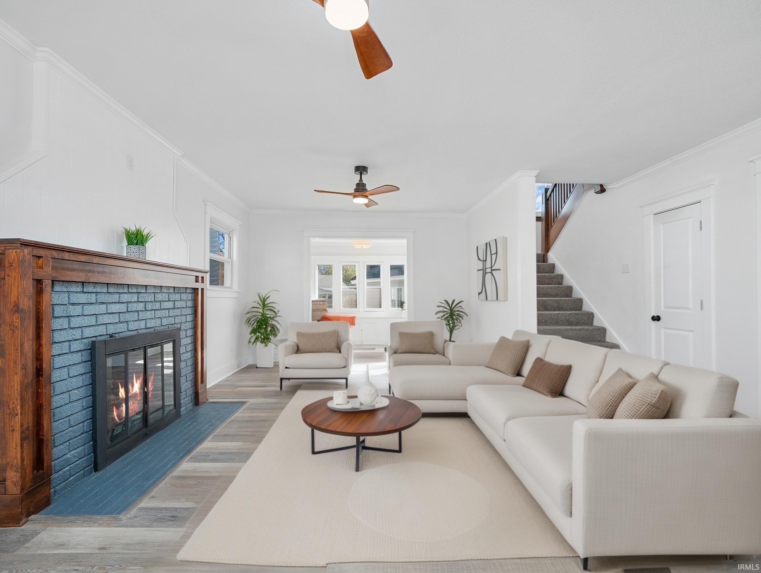 Living area with ornamental molding, wood finished floors, stairs, a brick fireplace, and a ceiling fan