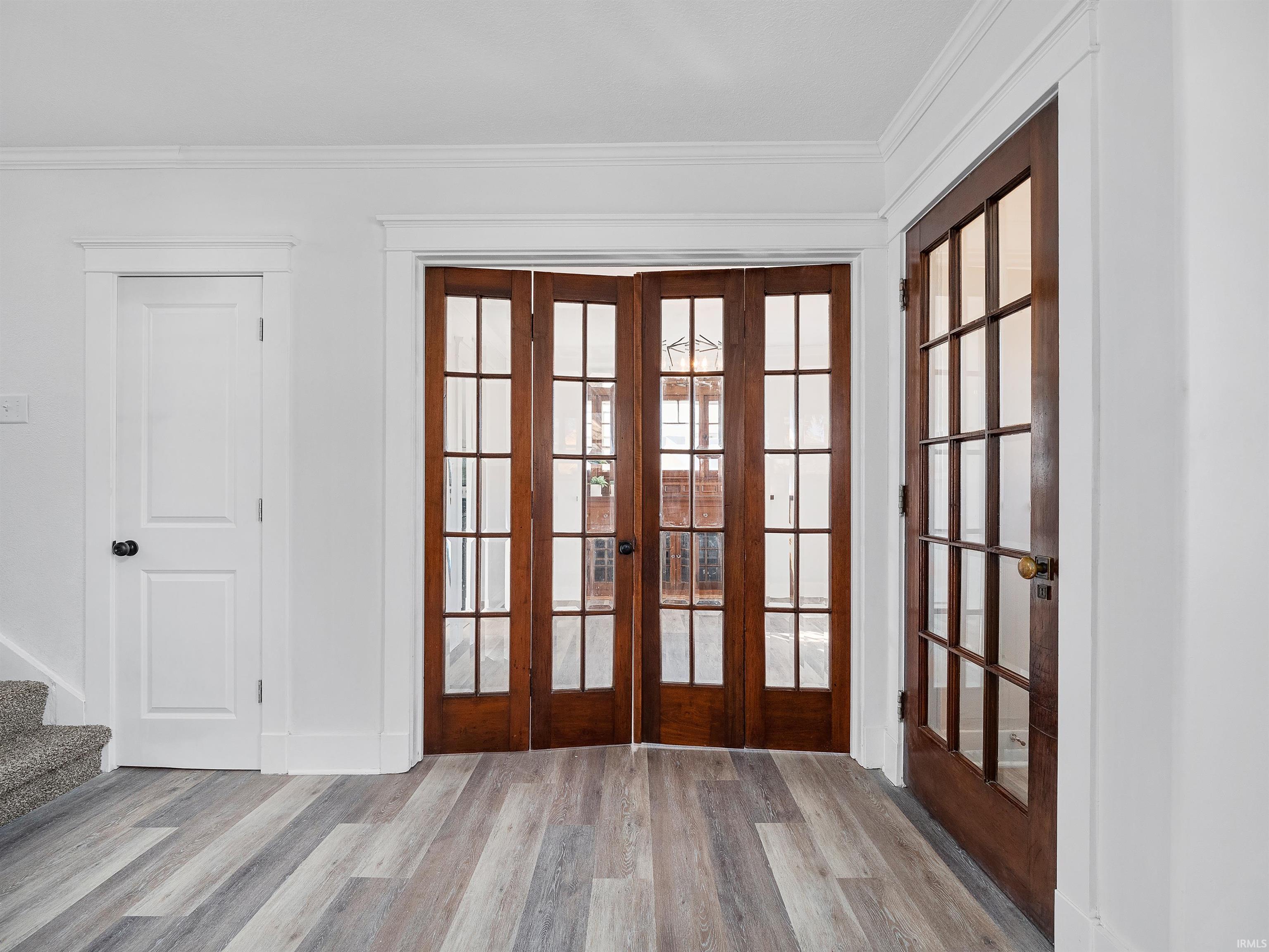 Doorway with french doors, wood finished floors, ornamental molding, and stairs