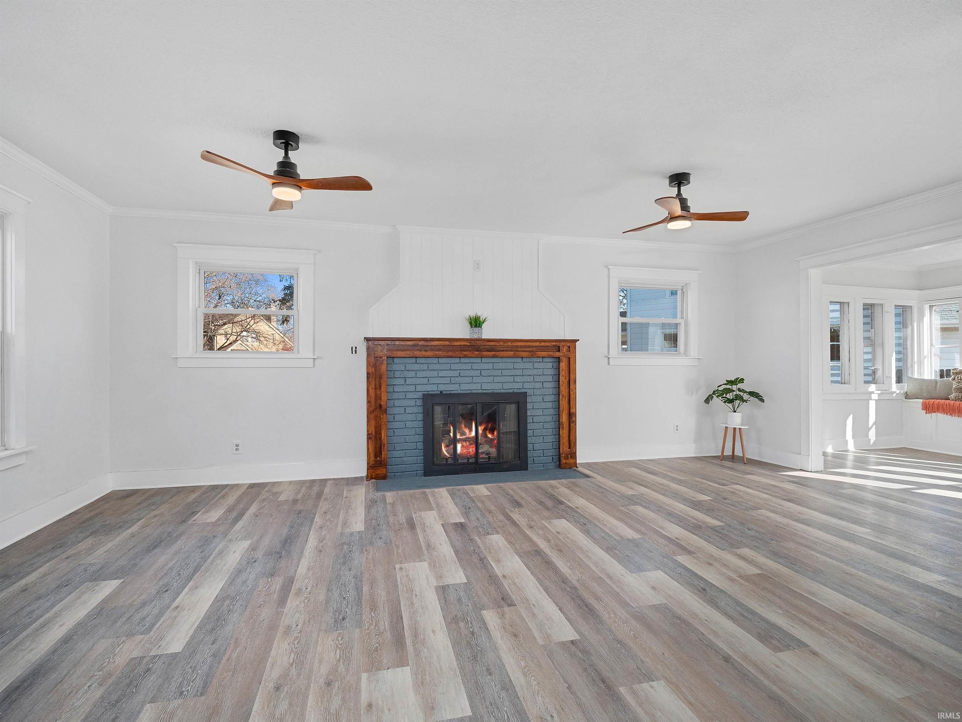 Unfurnished living room featuring crown molding, ceiling fan, light wood-style floors, and a fireplace