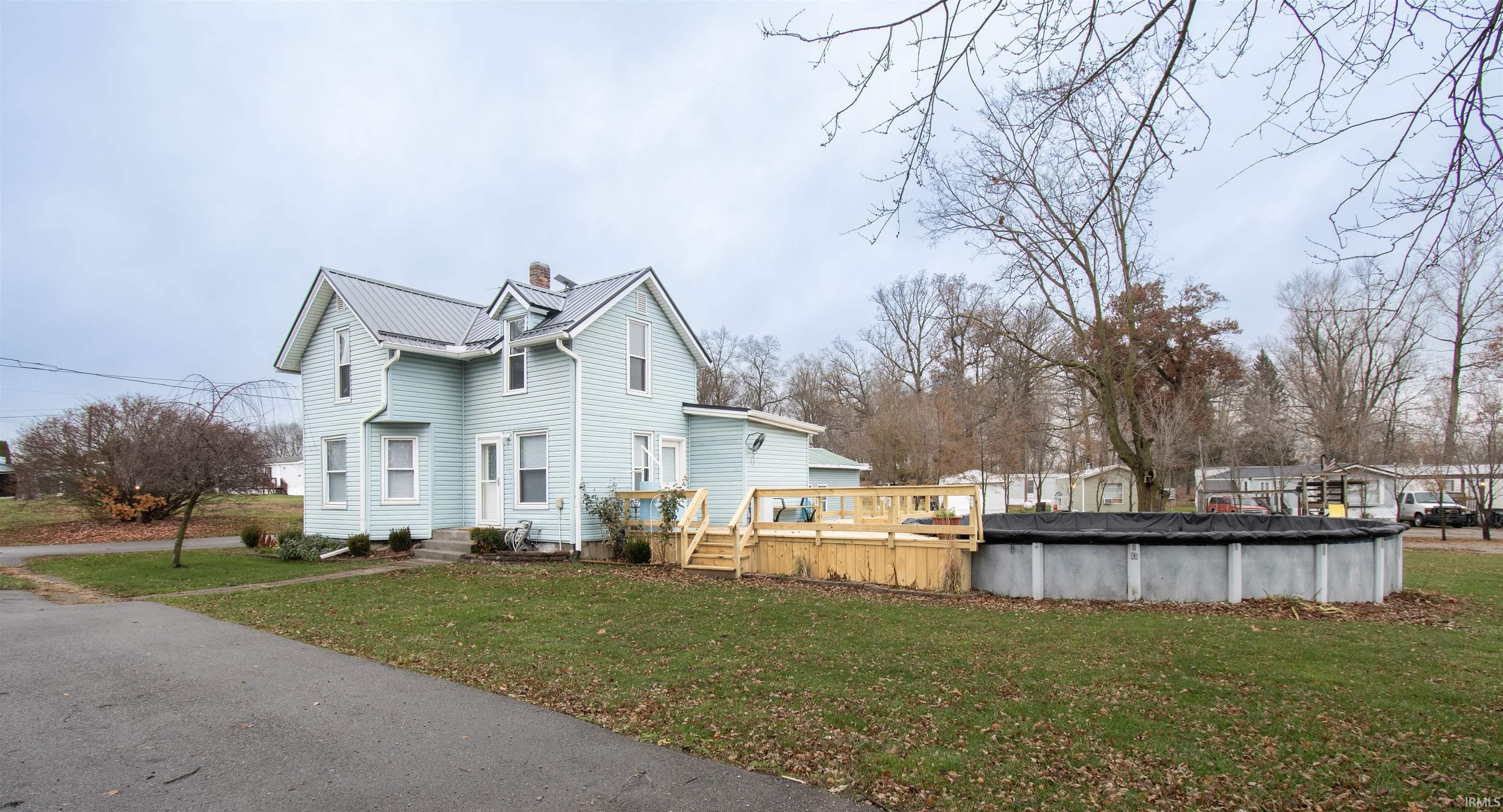 View of home's exterior with a lawn, a wooden deck, a chimney, a metal roof, and a covered pool