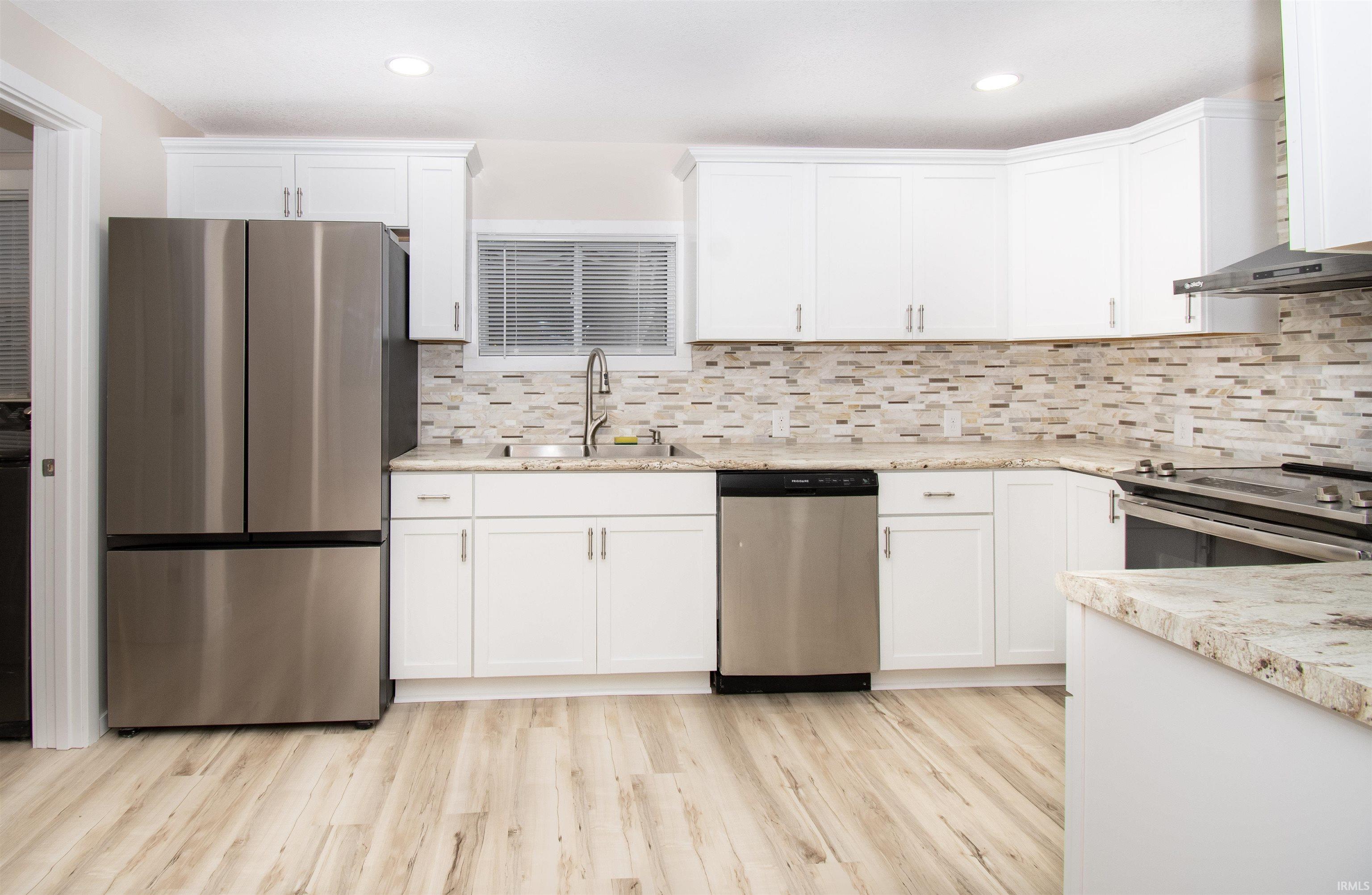 Kitchen with stainless steel appliances, wall chimney range hood, white cabinets, light wood-style floors, and recessed lighting