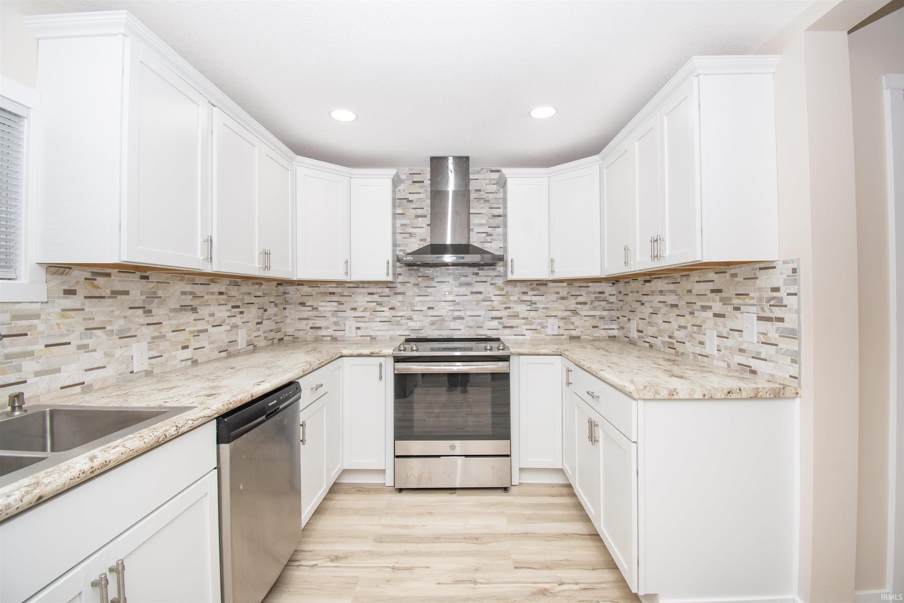Kitchen featuring stainless steel appliances, wall chimney range hood, white cabinets, light wood-type flooring, and light stone countertops