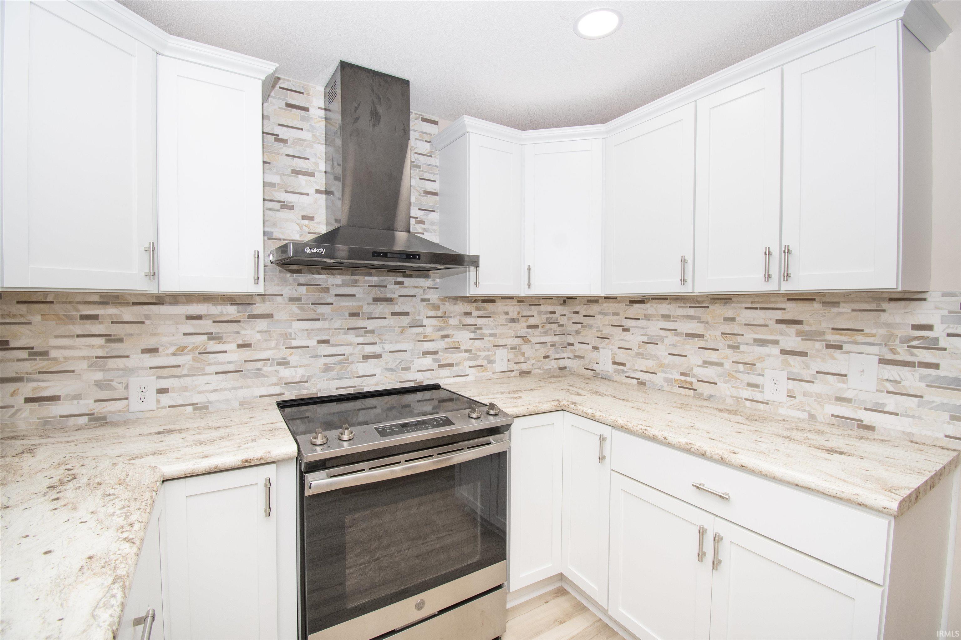 Kitchen featuring stainless steel range with electric cooktop, wall chimney range hood, white cabinetry, tasteful backsplash, and light stone countertops