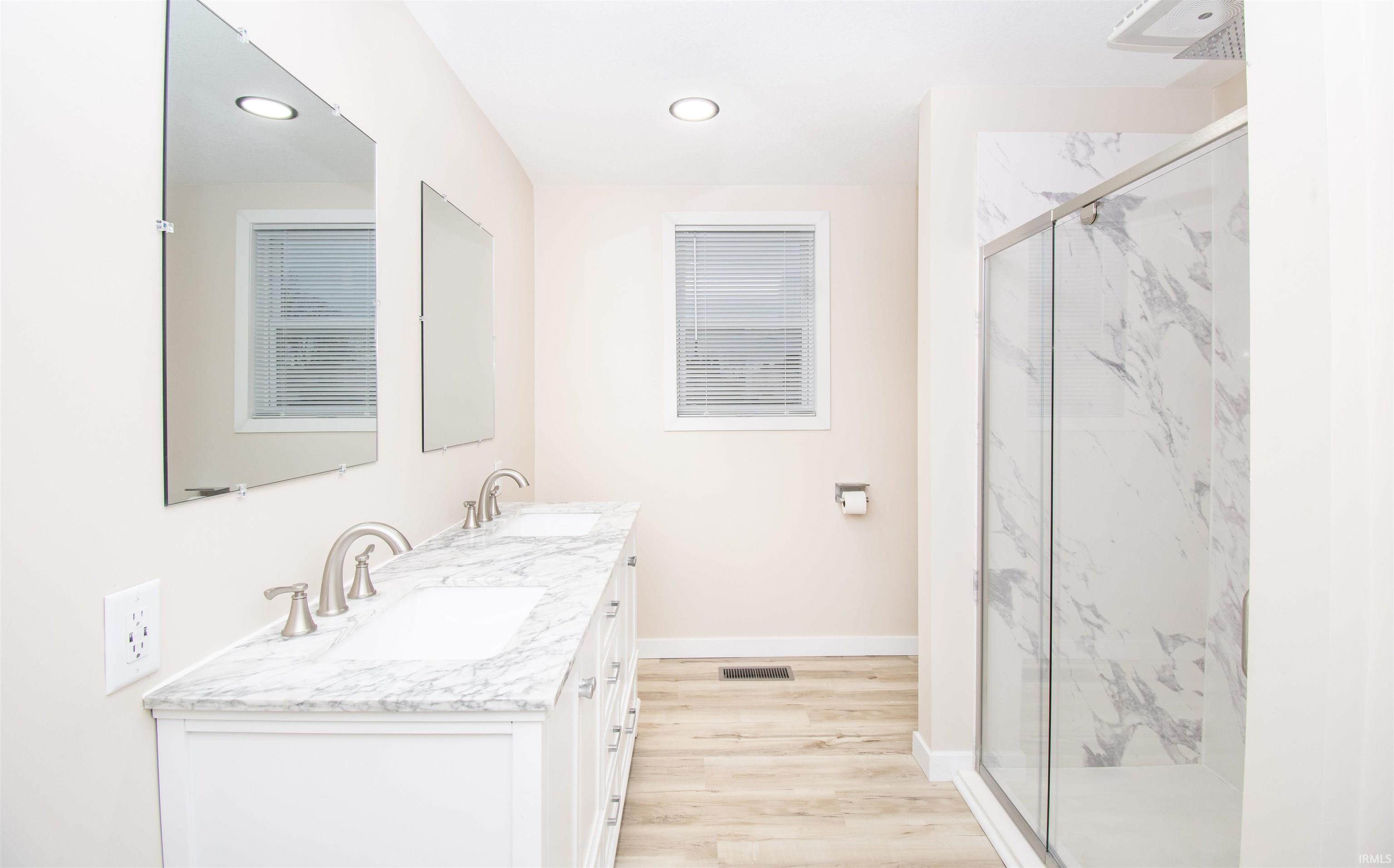 Bathroom featuring a marble finish shower, double vanity, light wood finished floors, and recessed lighting