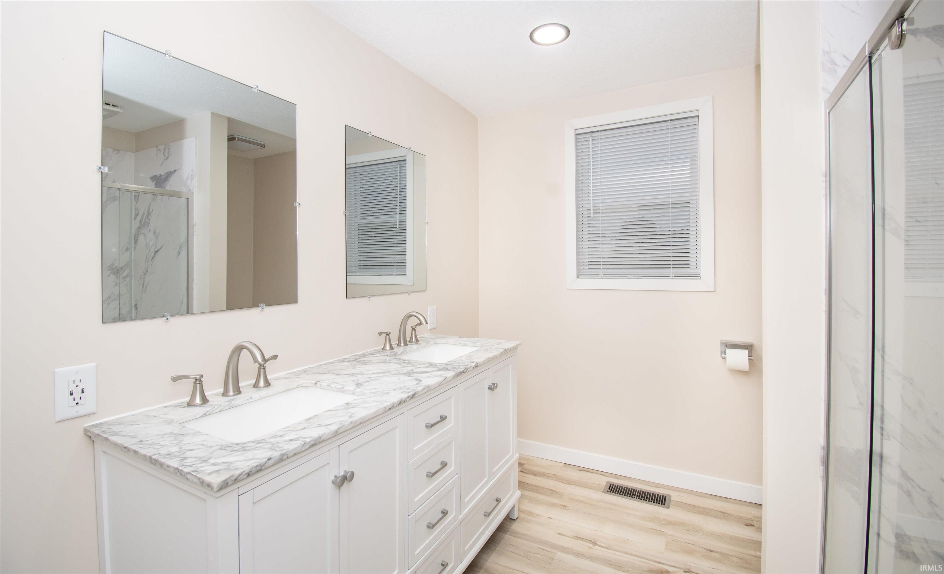 Bathroom with a marble finish shower, double vanity, and light wood-type flooring