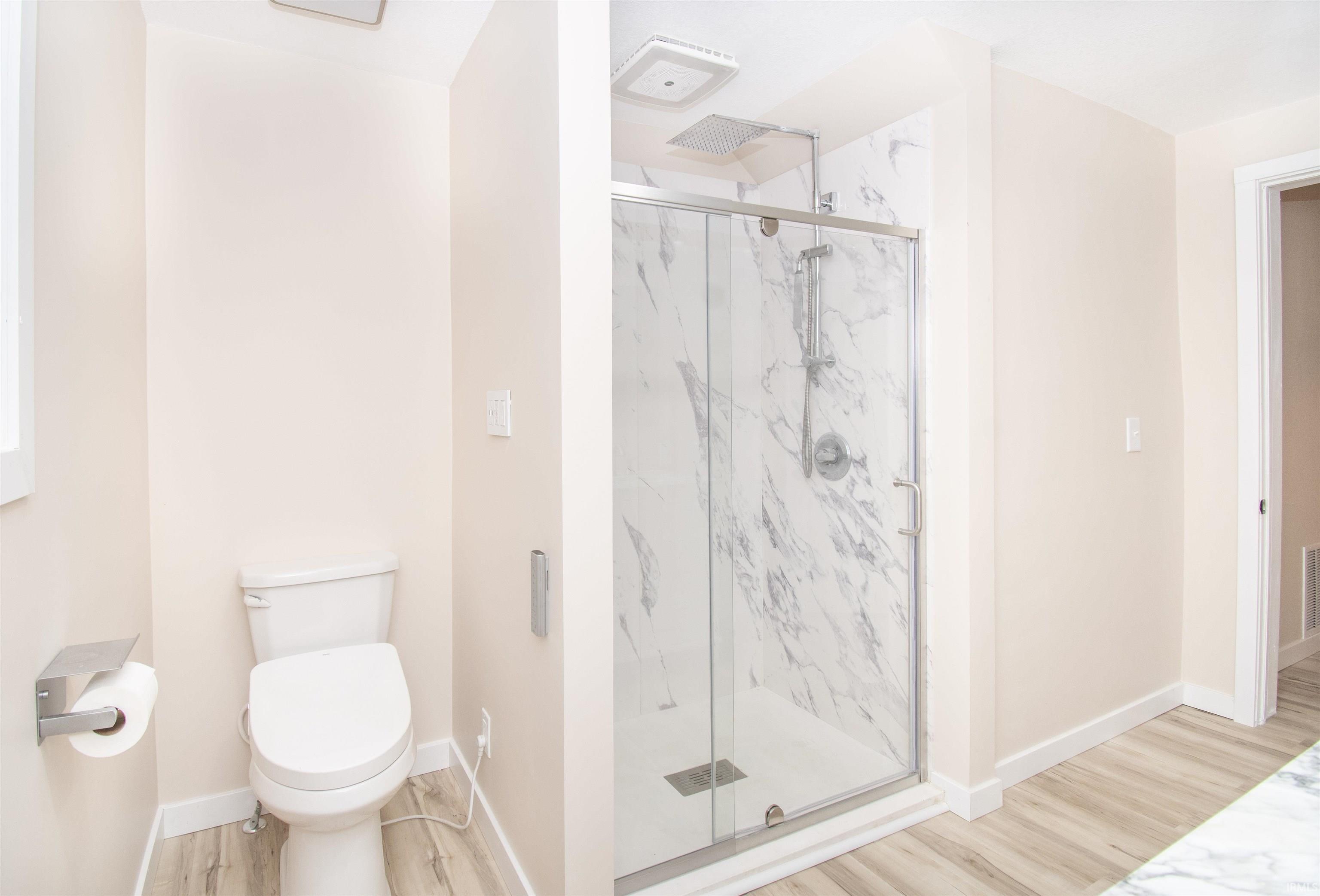 Full bathroom featuring a marble finish shower and light wood-style floors