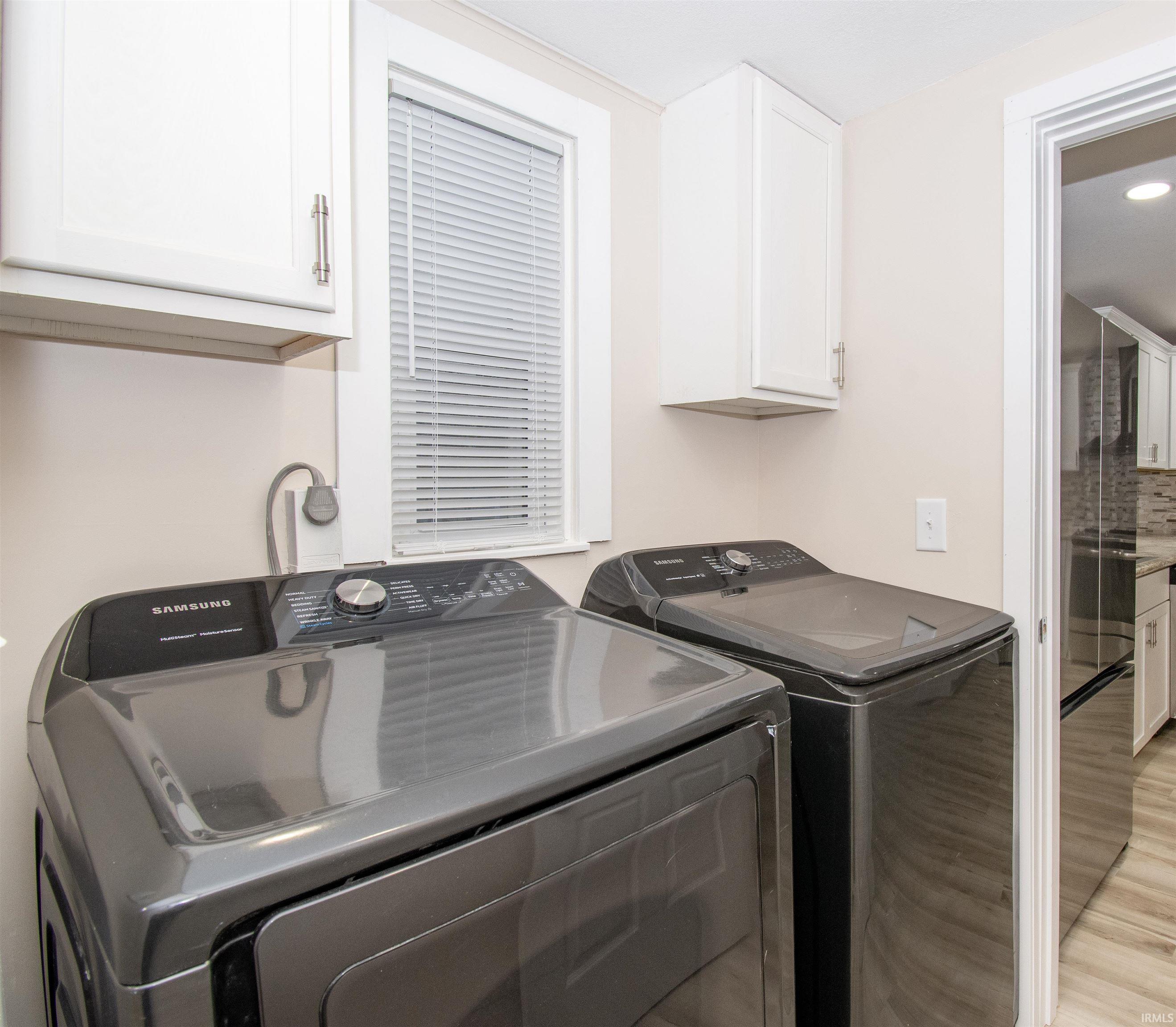 Laundry area featuring washer and clothes dryer, cabinet space, and light wood-style floors