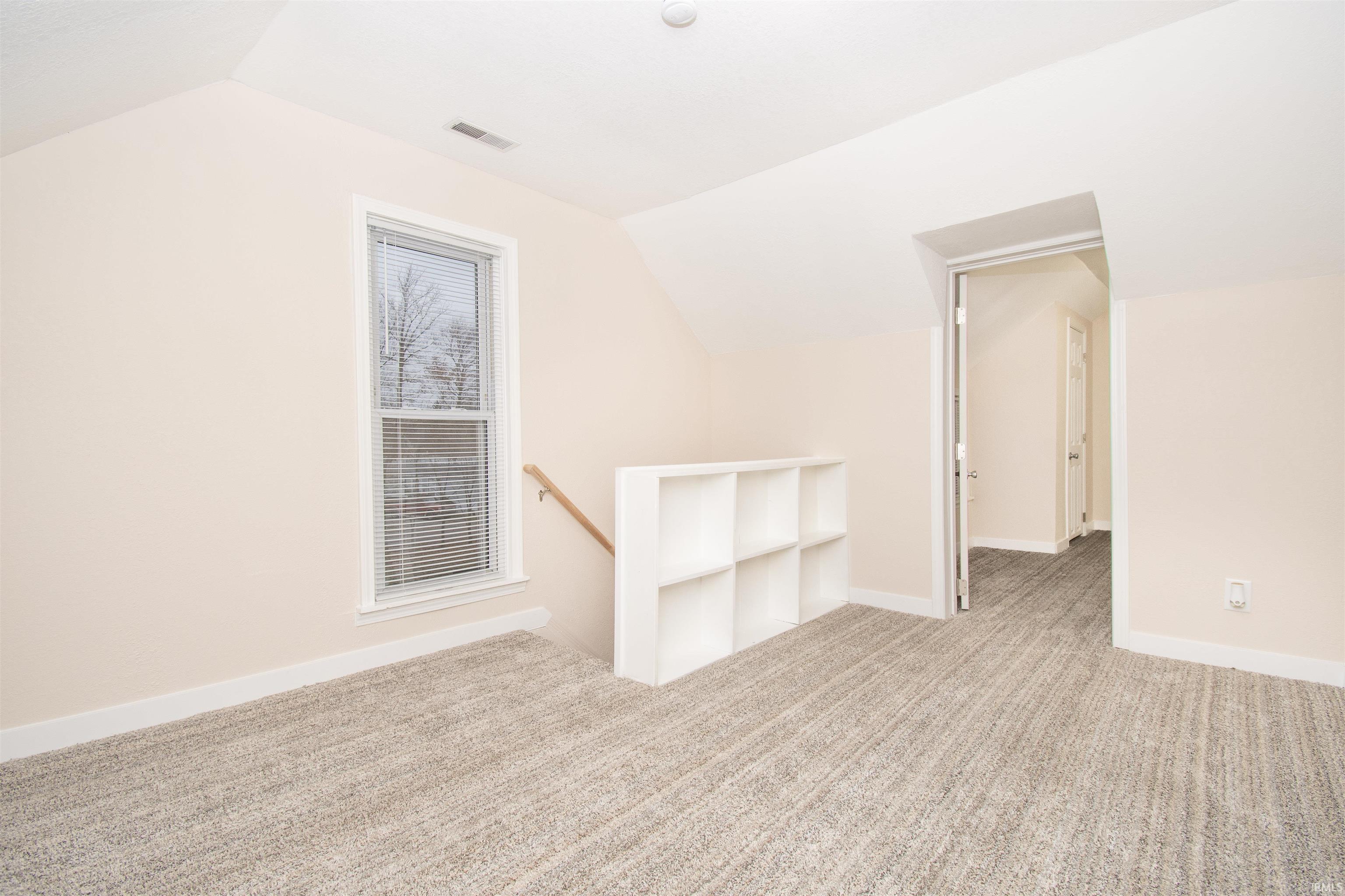 Empty room with lofted ceiling and light colored carpet