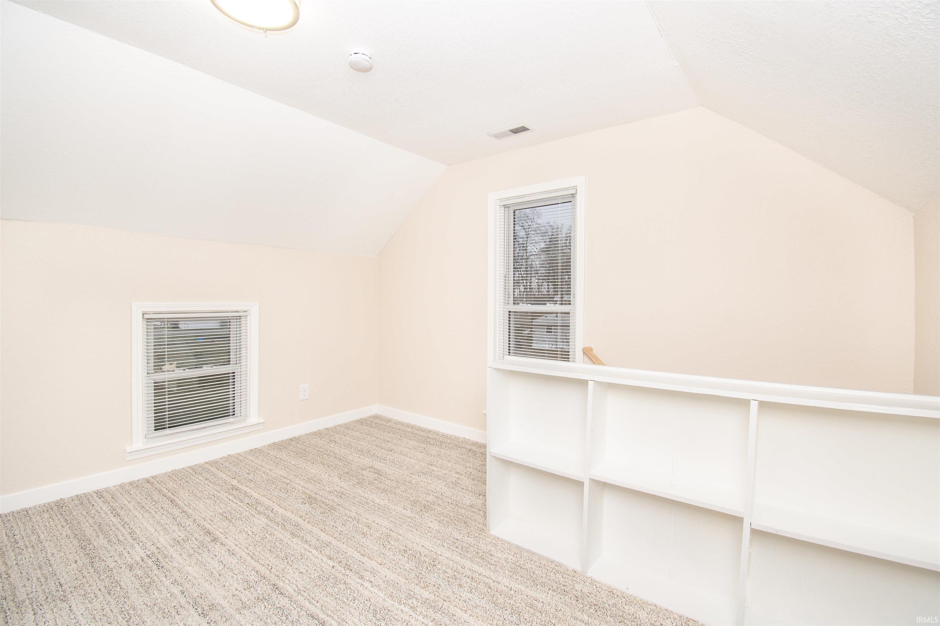 Bonus room with vaulted ceiling and light colored carpet
