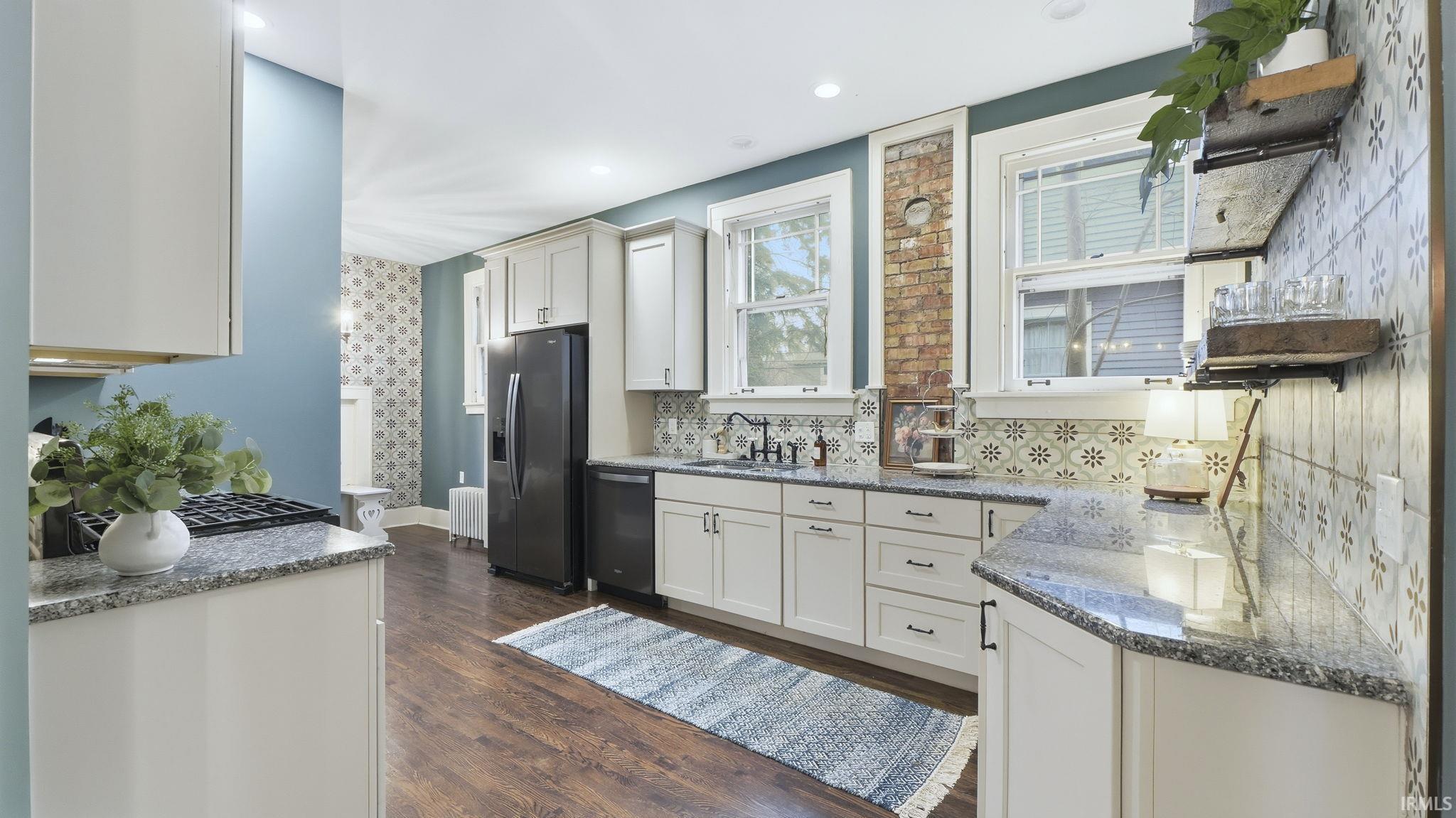 Kitchen with wallpapered walls, light stone counters, appliances with stainless steel finishes, dark wood-style flooring, and radiator heating unit