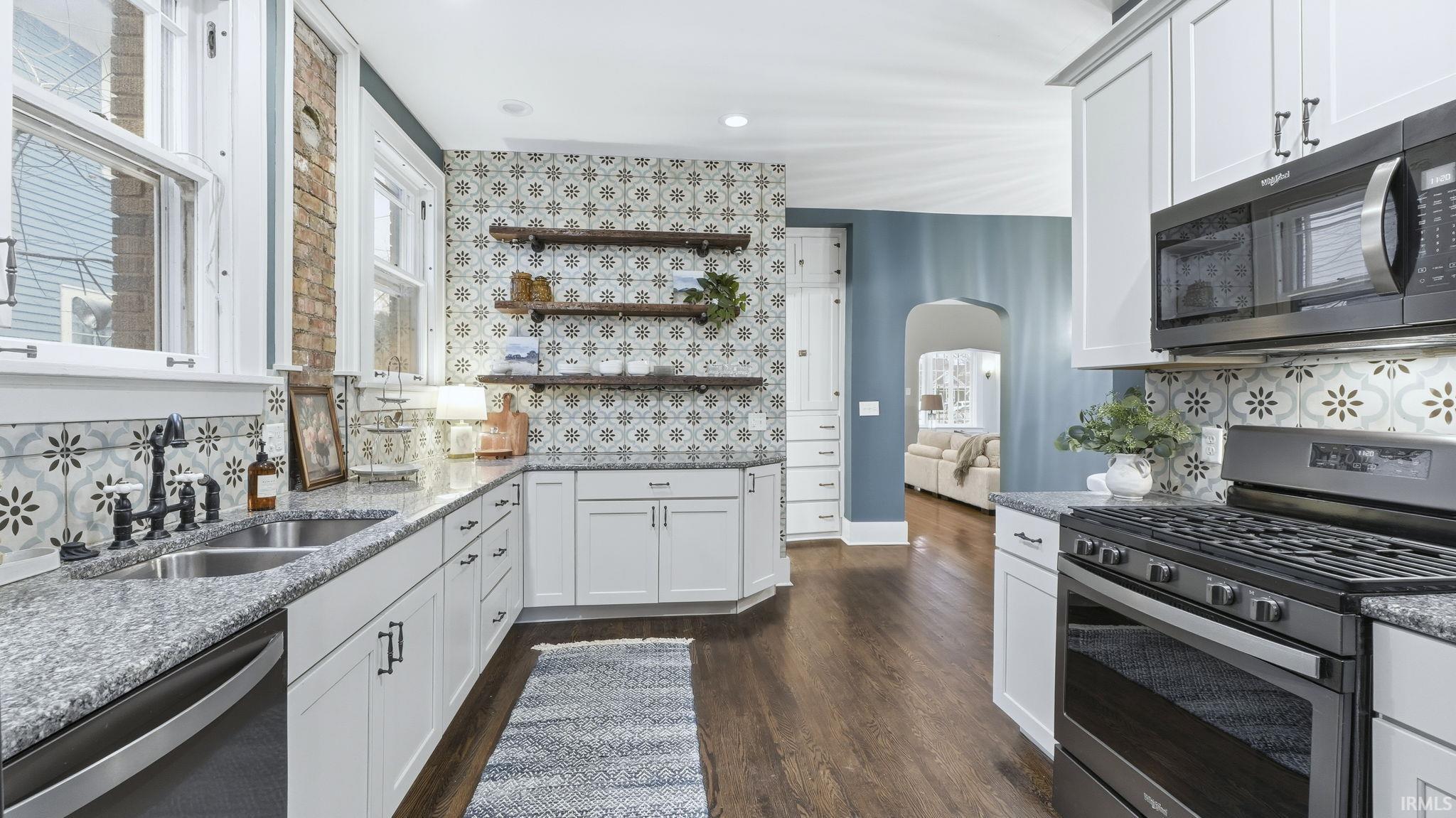 Kitchen with stainless steel appliances, arched walkways, decorative backsplash, white cabinetry, and recessed lighting