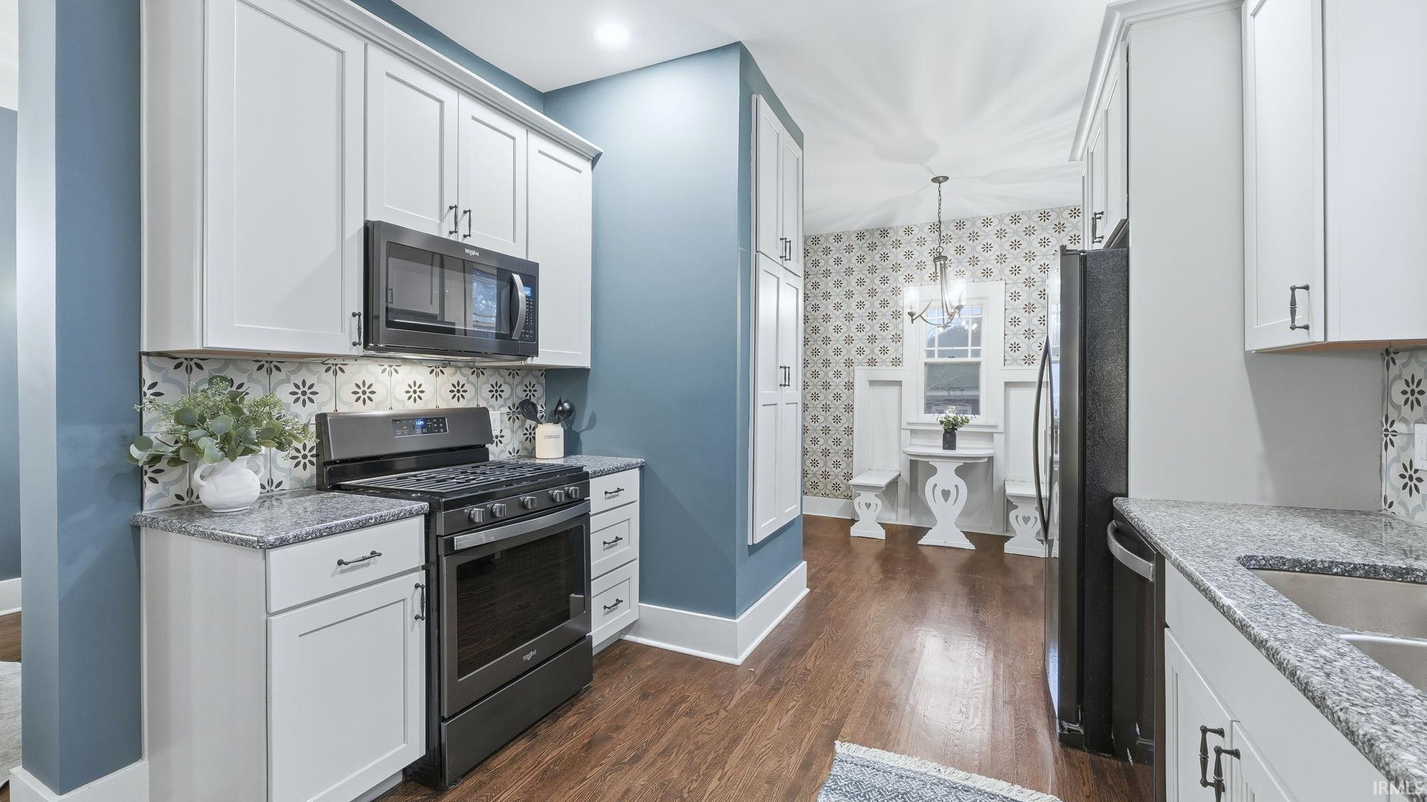 Kitchen featuring wallpapered walls, appliances with stainless steel finishes, a chandelier, hanging light fixtures, and dark wood-style floors